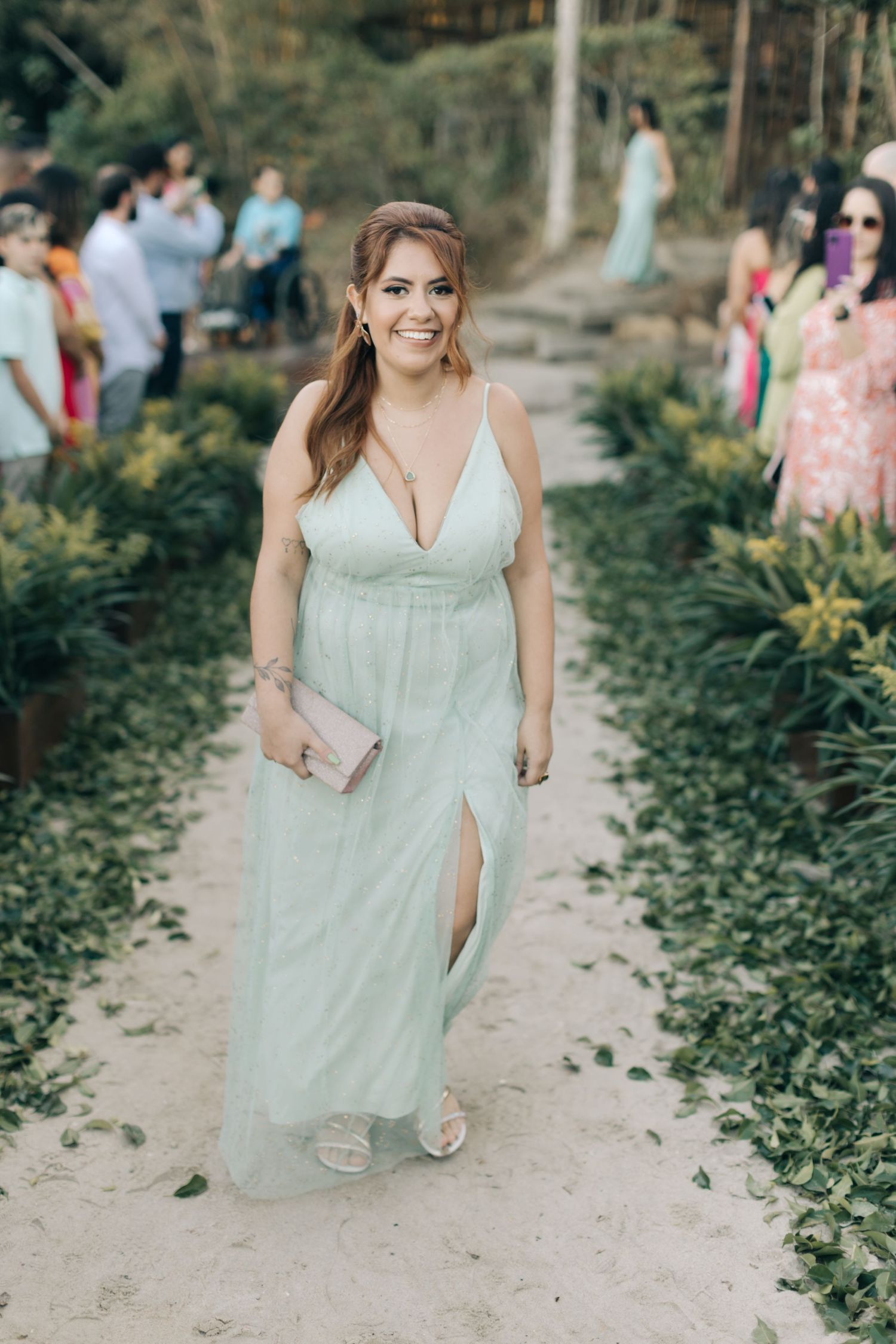 A bridesmaid in a mint green dress walks along a garden path during a wedding celebration.