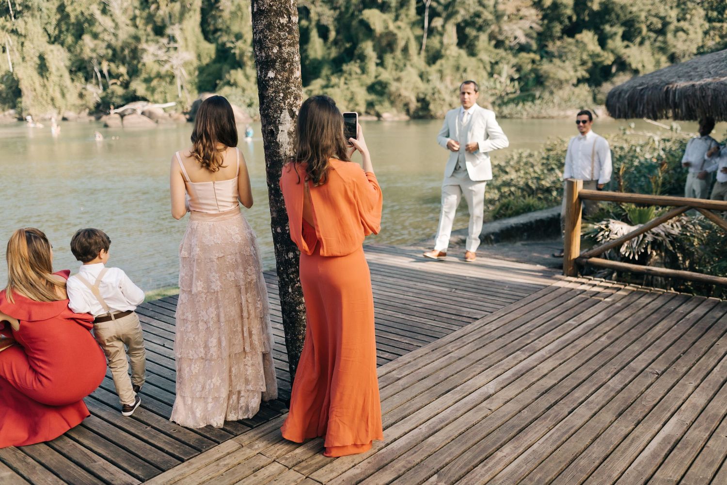 Wedding guests gathered on wooden deck by waterfront during outdoor celebration.