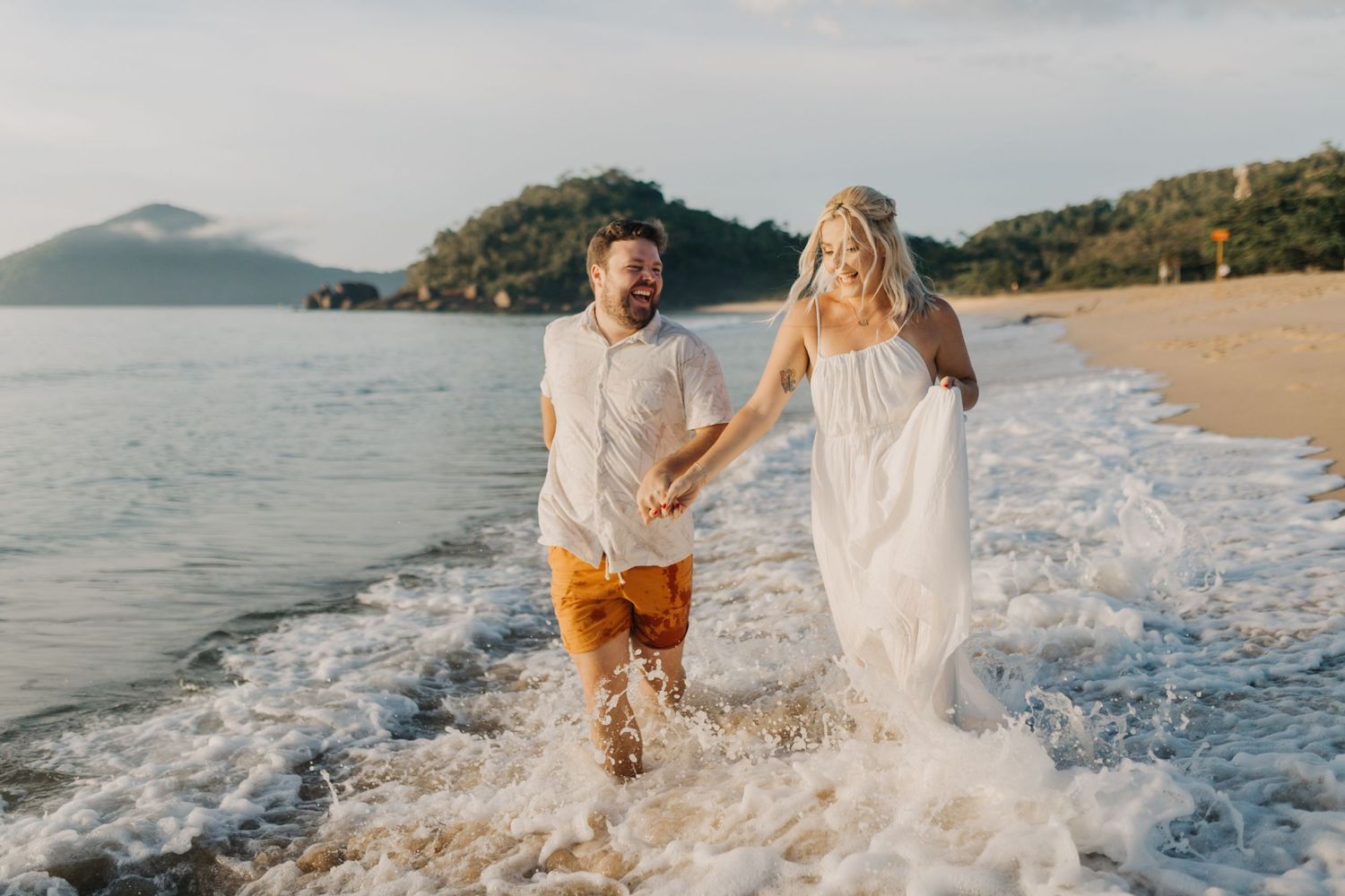 Couple playing and splashing in ocean waves at sunset on a tropical beach.