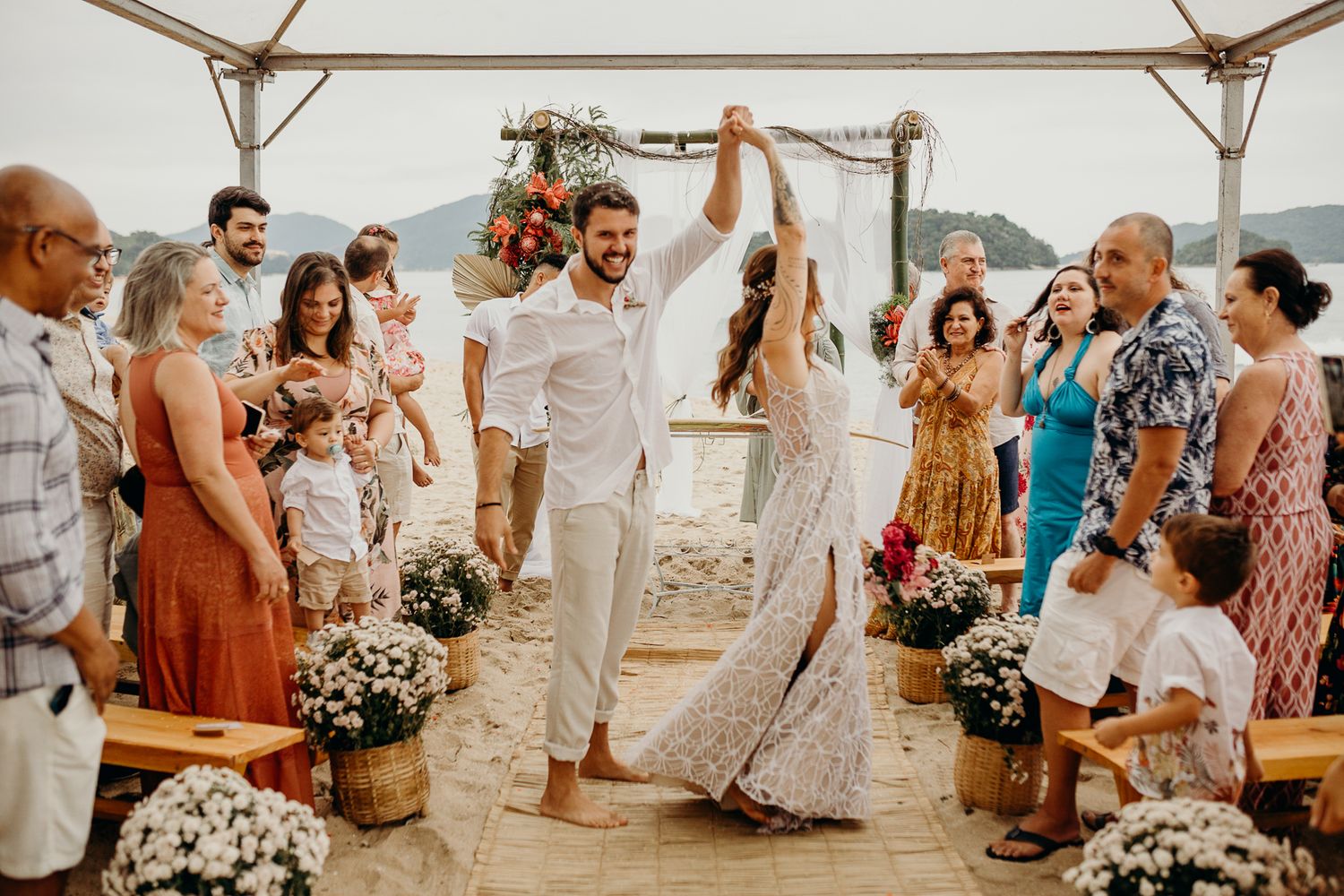 A beach wedding ceremony with guests gathered under a canopy by the ocean.