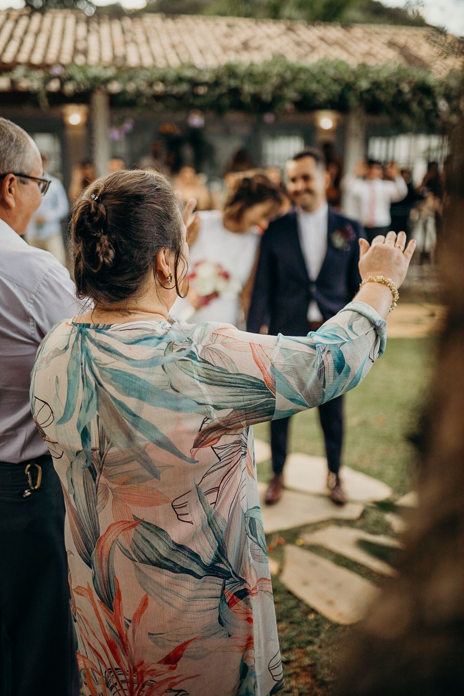 A guest gestures enthusiastically during an outdoor wedding ceremony under a covered patio.