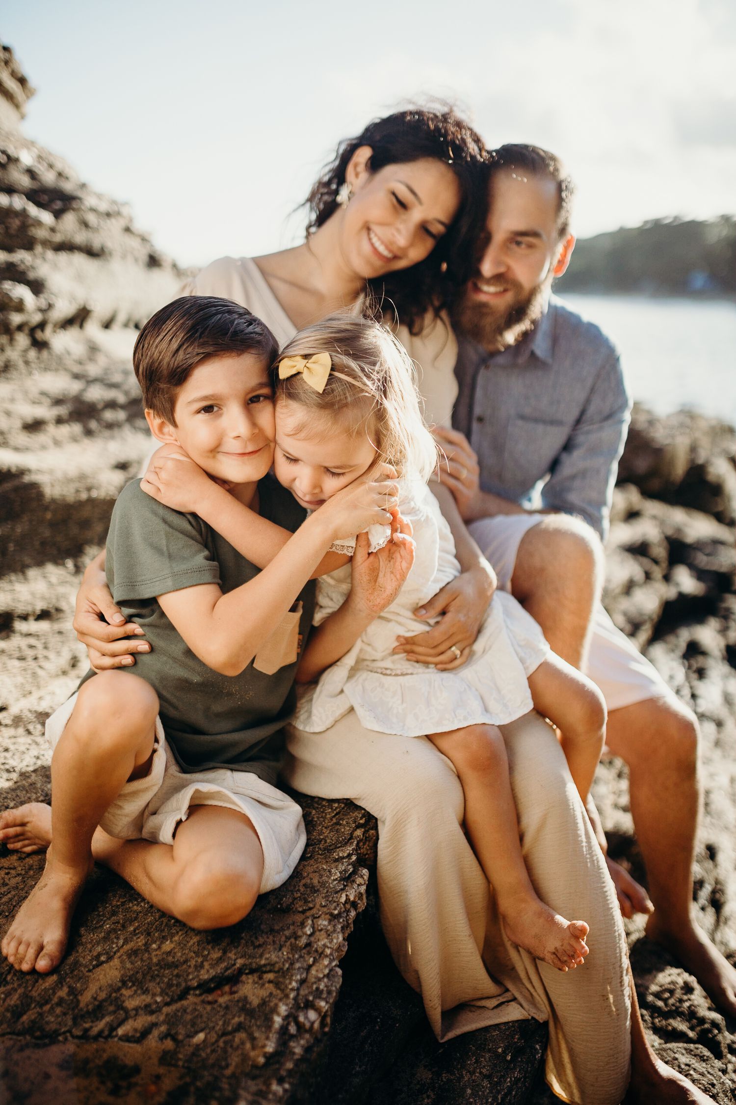 Family members share joyful embraces while sitting together on coastal rocks.