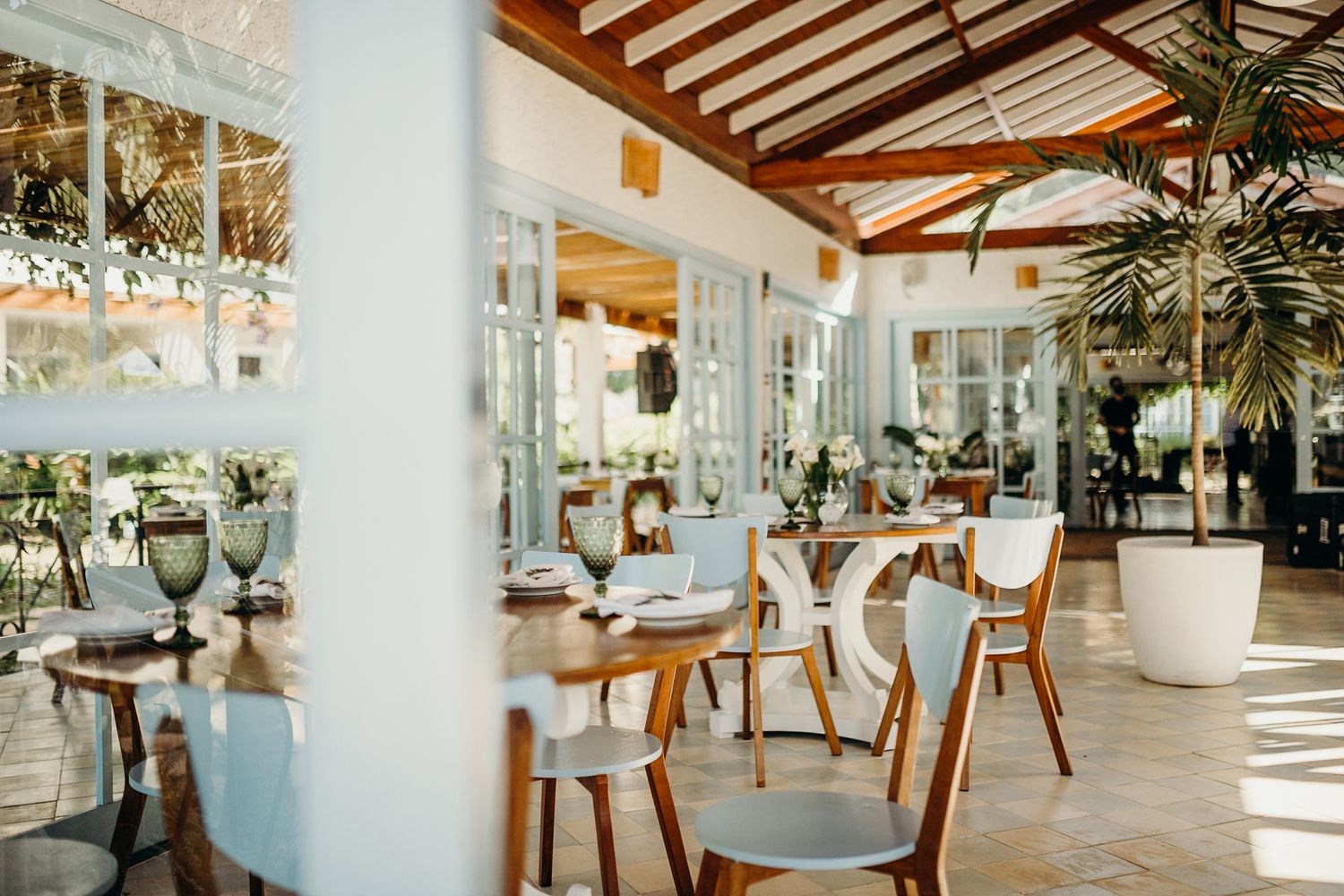Bright indoor dining area with white columns, wooden chairs, and natural sunlight streaming in.