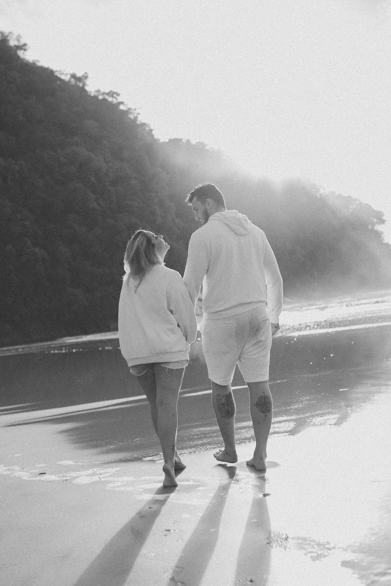 Black and white image of a couple walking together on a misty beach at sunset.