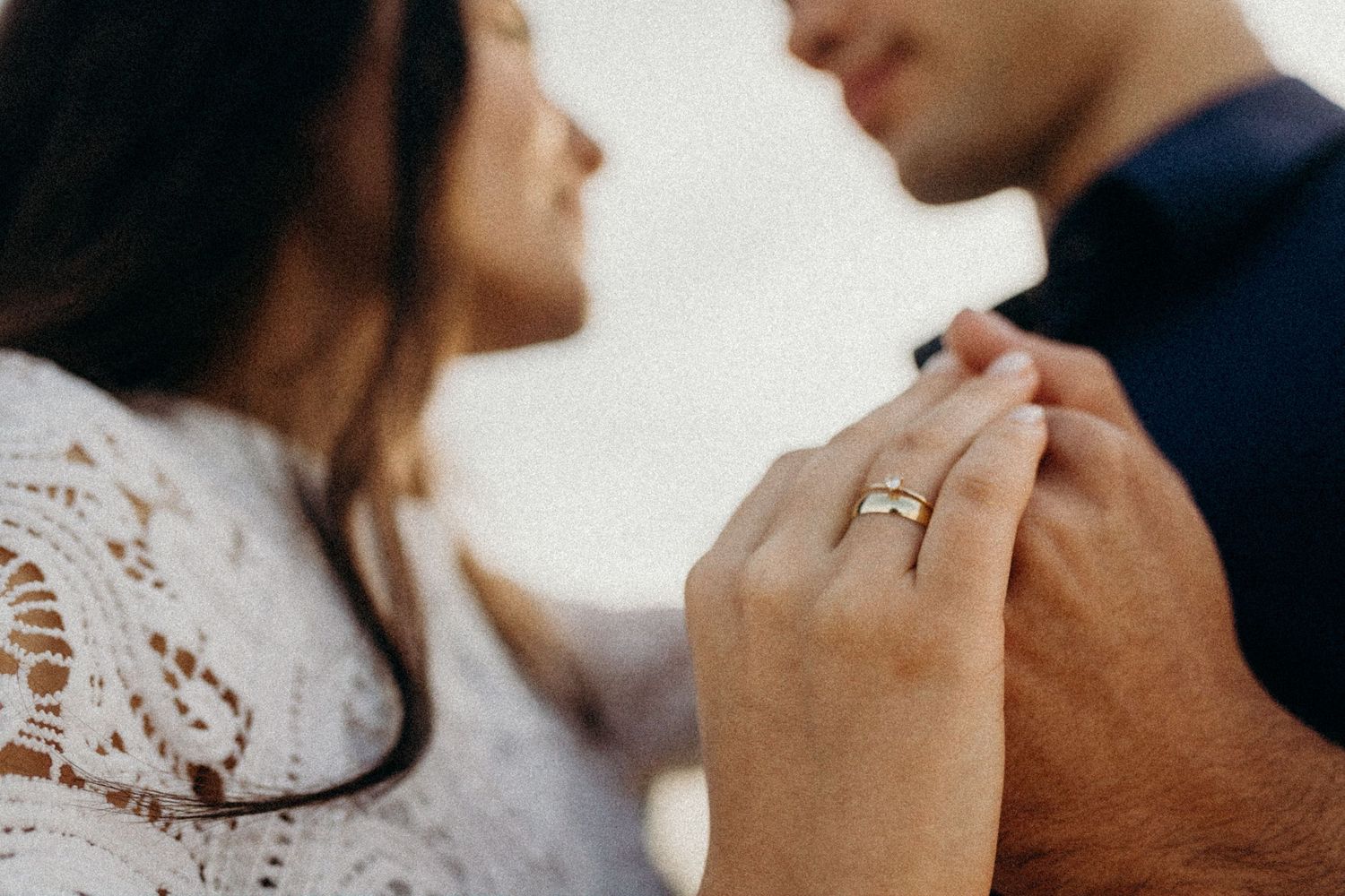 A romantic couple embraces during their engagement session wearing white lace and navy blue attire.