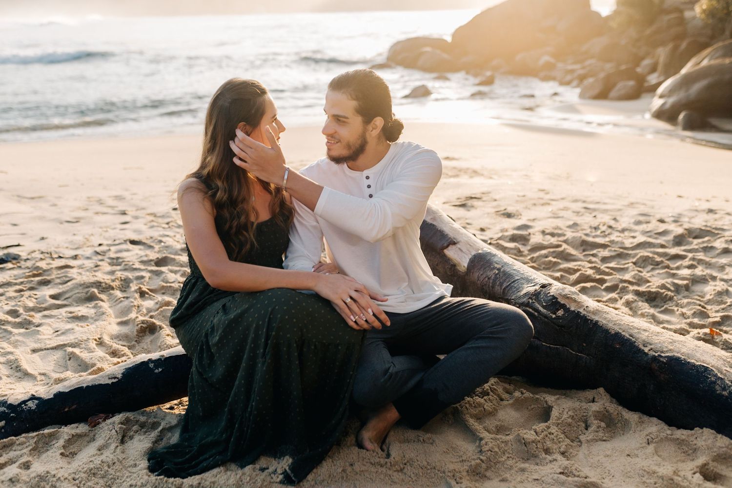 Couple sitting together on beach during sunset engagement session.