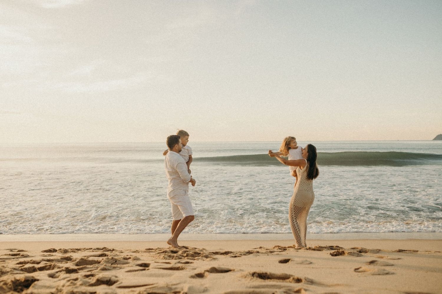 Two people enjoying playful moment with children on sunny beach.