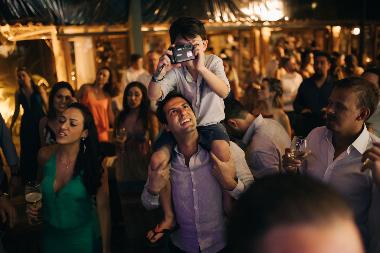 Wedding reception guests dancing and celebrating under warm ambient lighting.