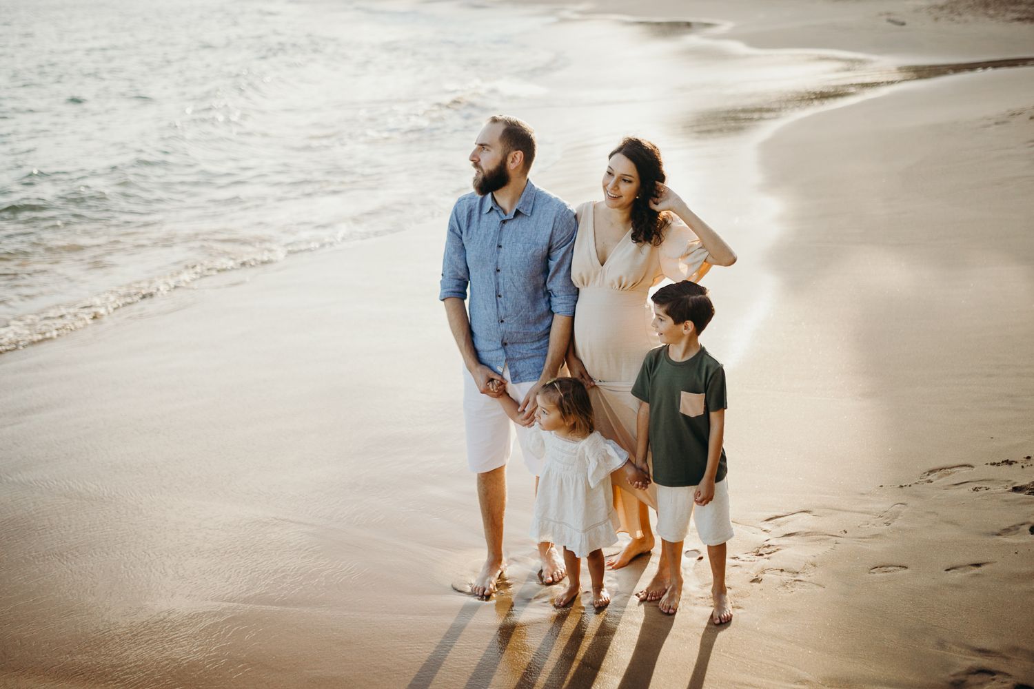 Family portrait on beach with gentle waves and golden evening light.