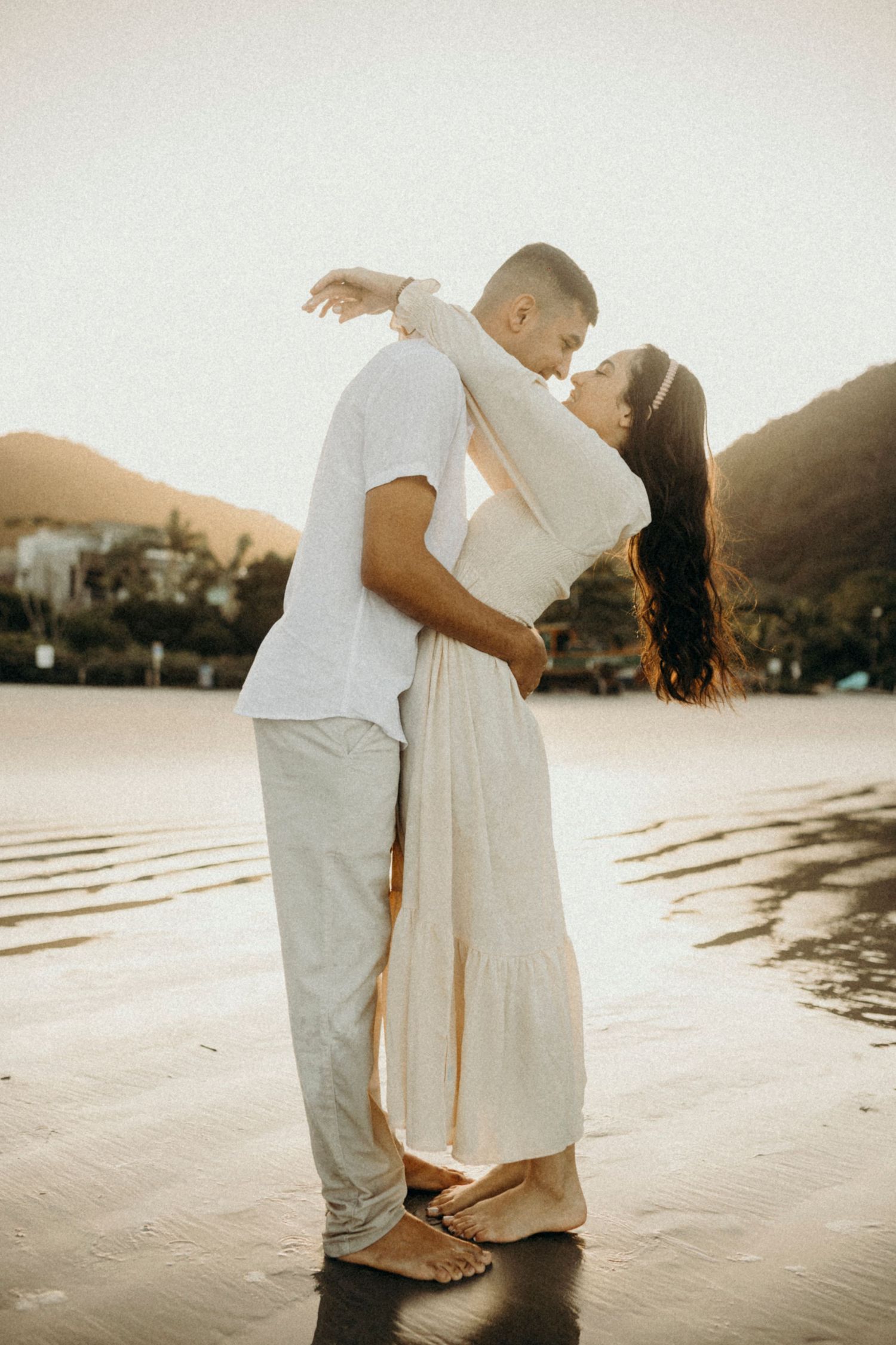 Couple in coordinated outfits dancing on beach during sunset.
