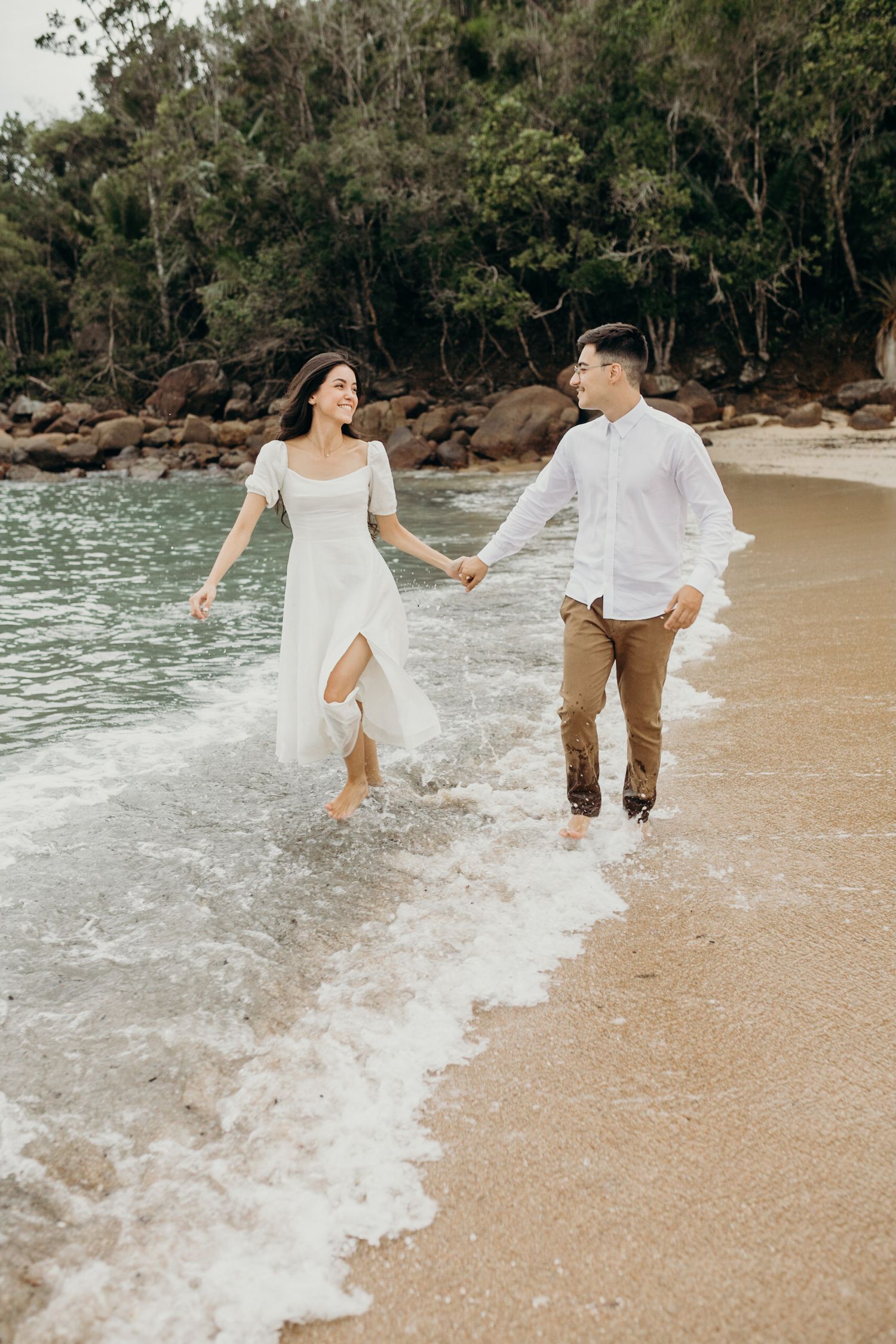 A couple plays in the ocean waves during their romantic beach photoshoot.