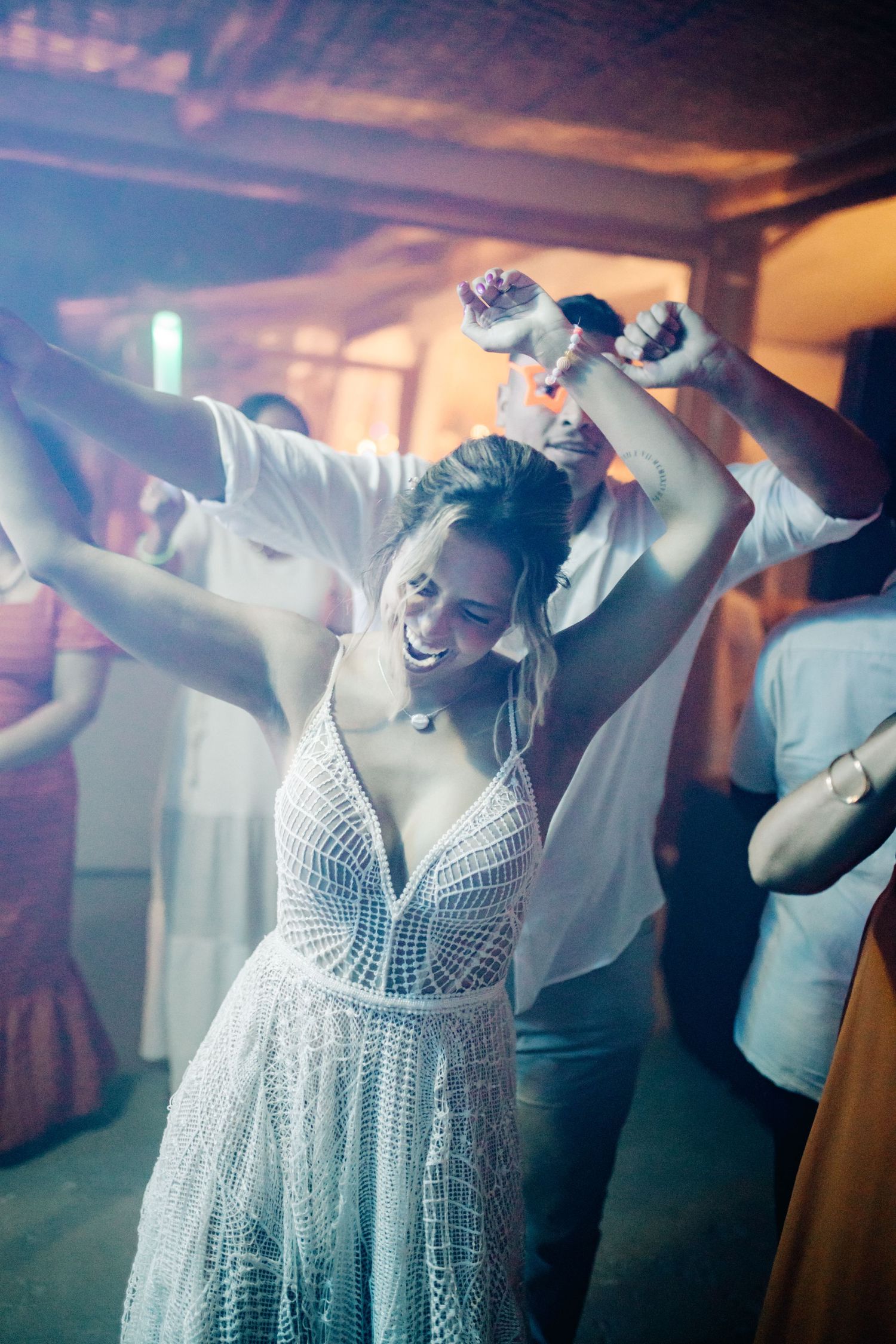 Person in white lace dress dances energetically at a party with arms raised.