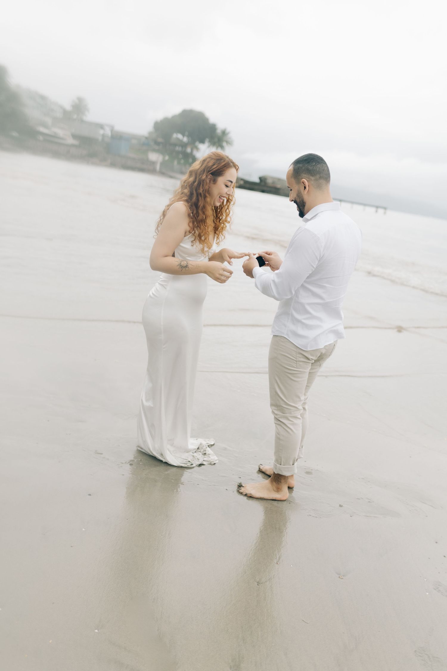 A romantic proposal moment unfolds on a cloudy beach with a person kneeling.