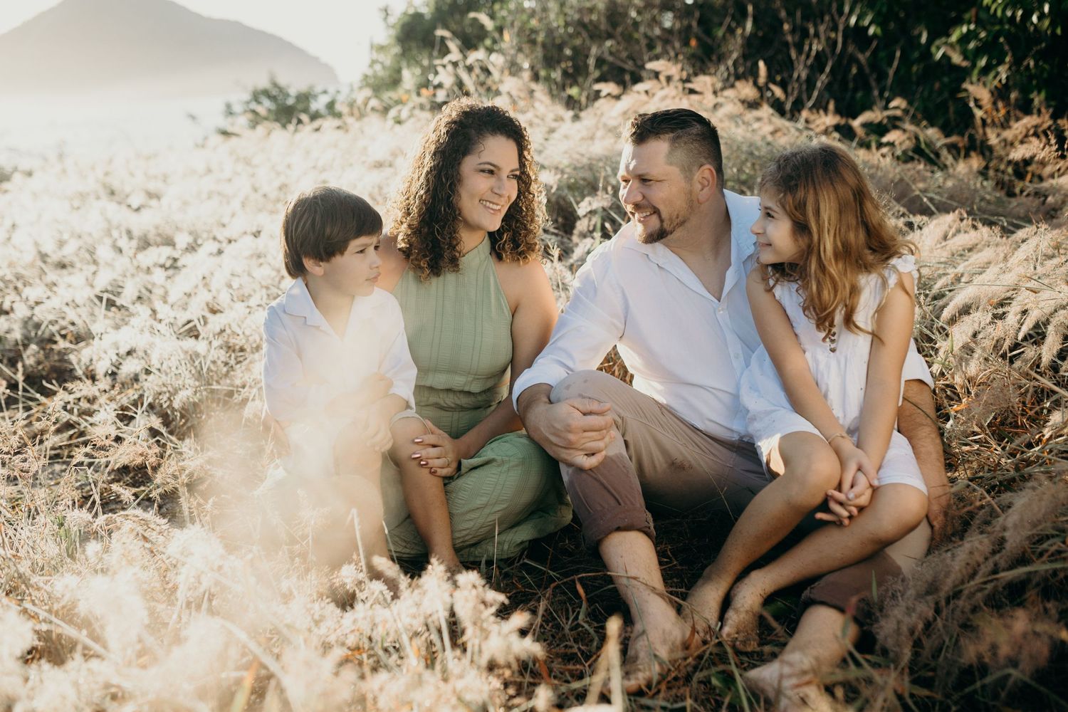 Candid family portrait of four people sitting together outdoors in natural golden light.