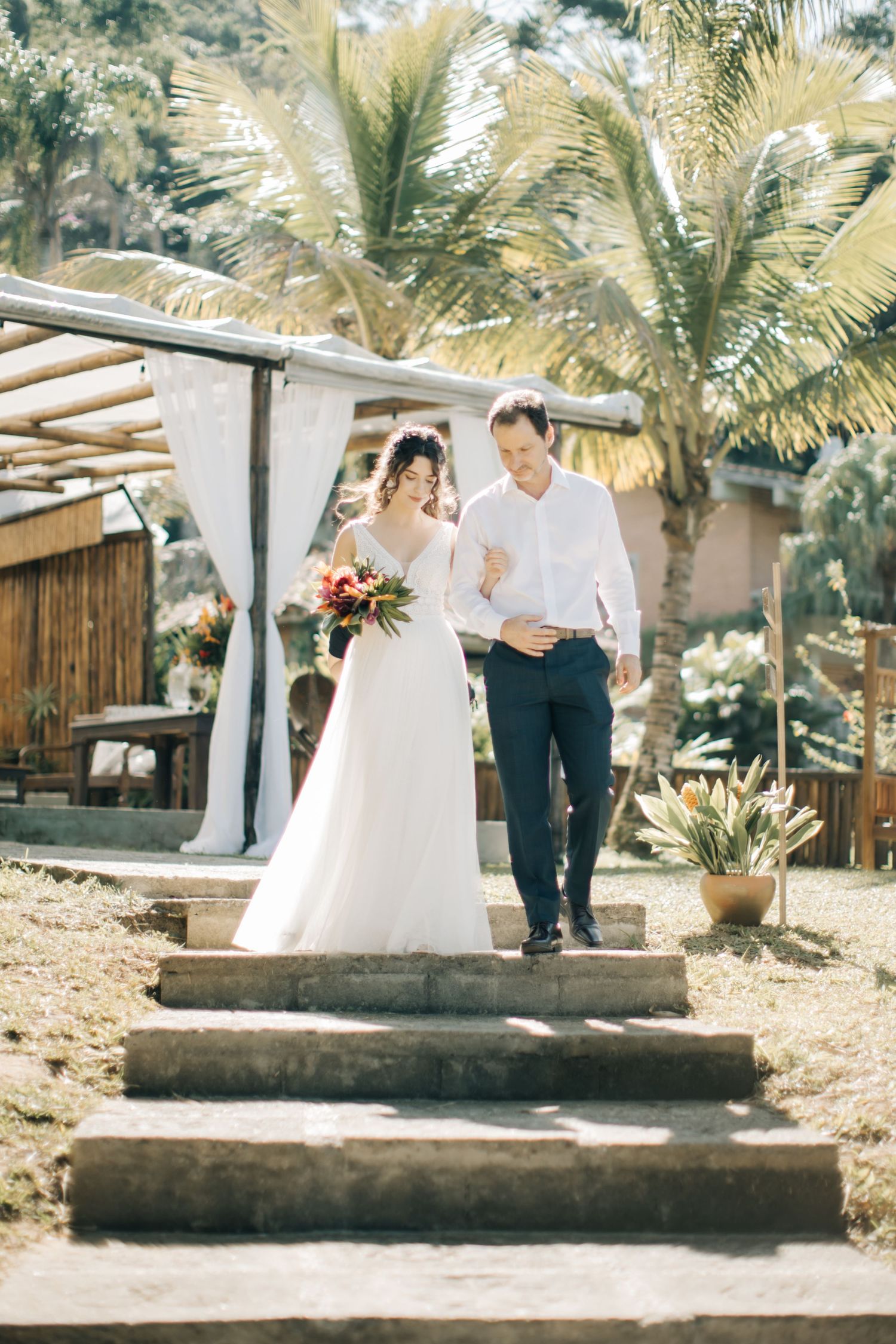 A couple descends stone steps surrounded by palm trees at their tropical destination wedding.