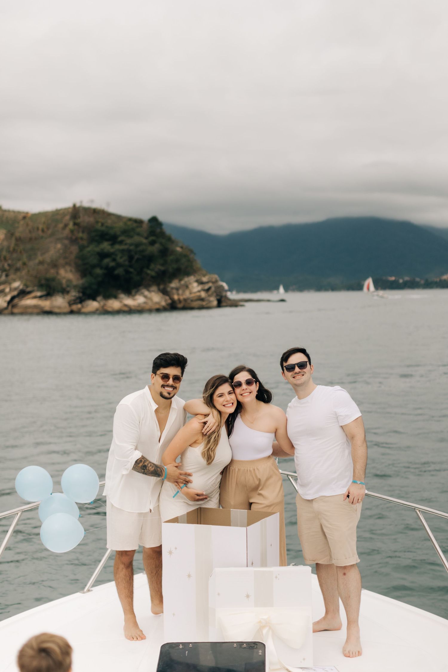 Friends gathered on a yacht's bow with balloons and mountains in the background.