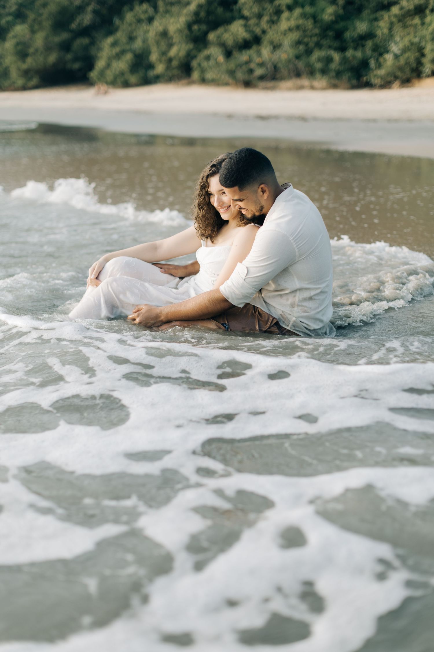 A romantic couple embracing while sitting in the shallow surf on a beach.