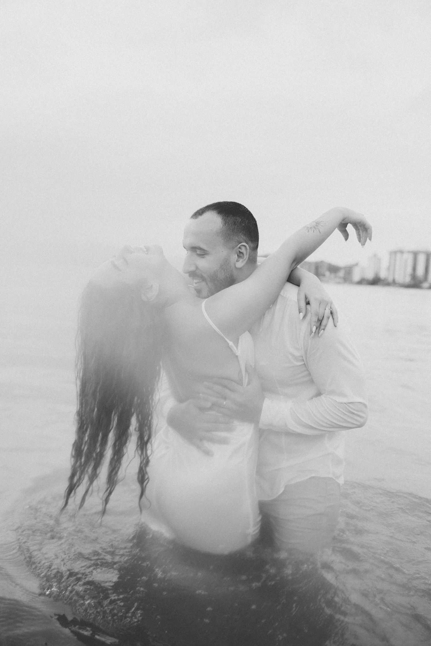 An artistic black and white photo captures a couple's intimate dance in the ocean.