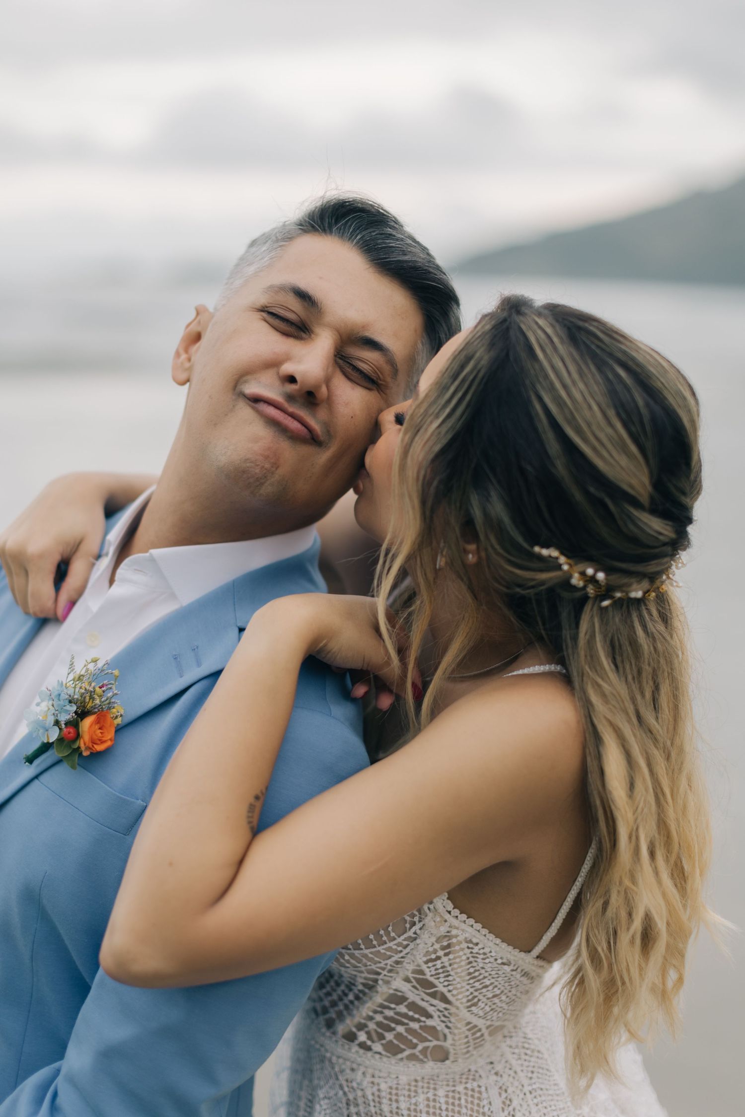 A couple in wedding attire laugh together during their beach photoshoot.