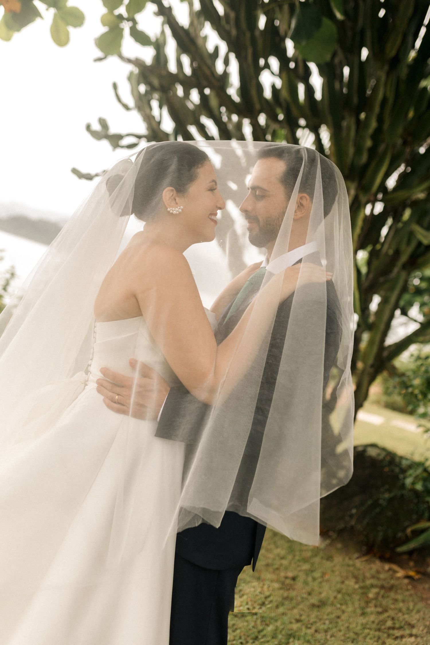 Intimate wedding portrait through sheer veil in garden setting.