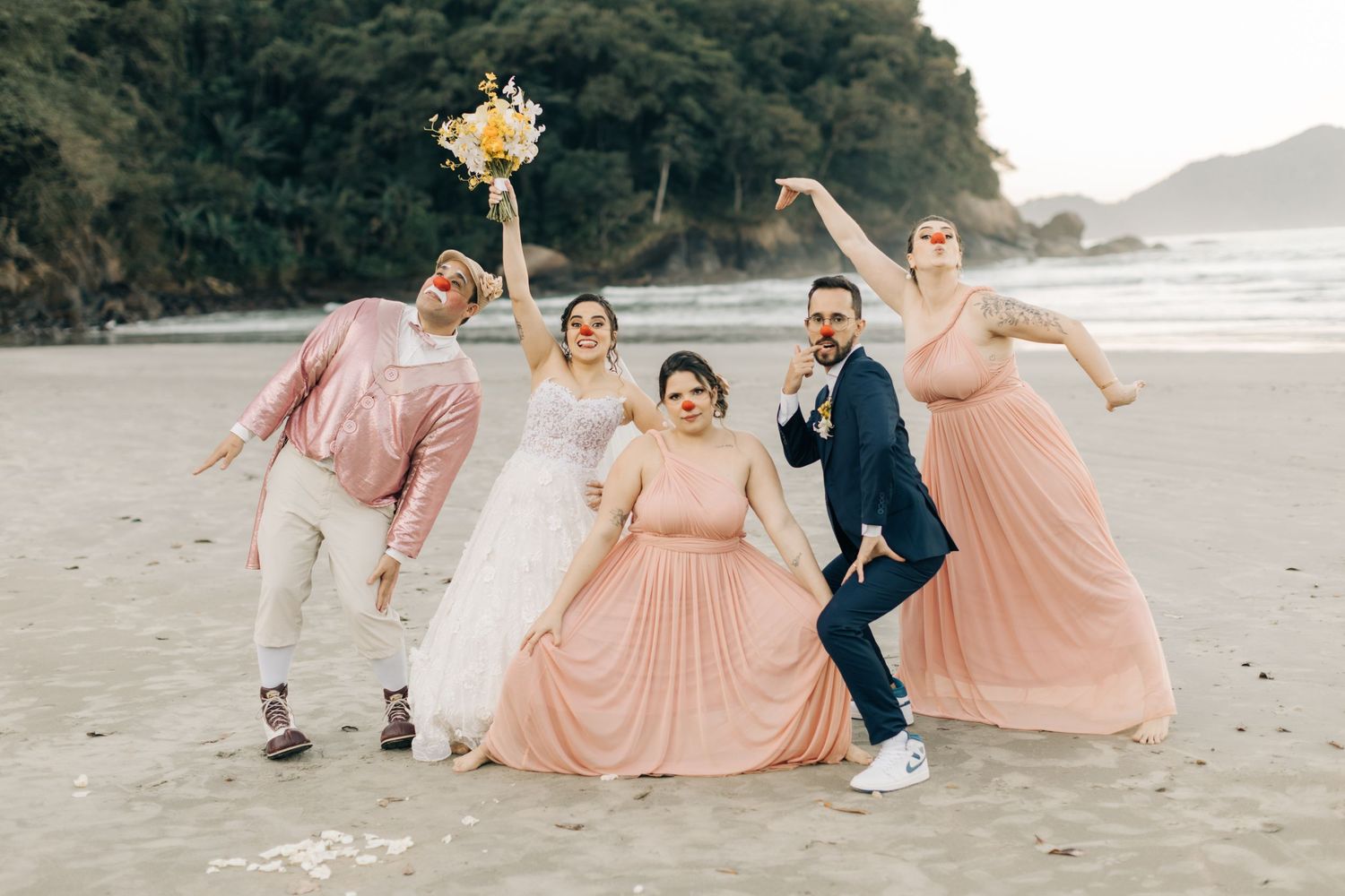 Wedding party in pink and navy attire posing playfully on a scenic beach.