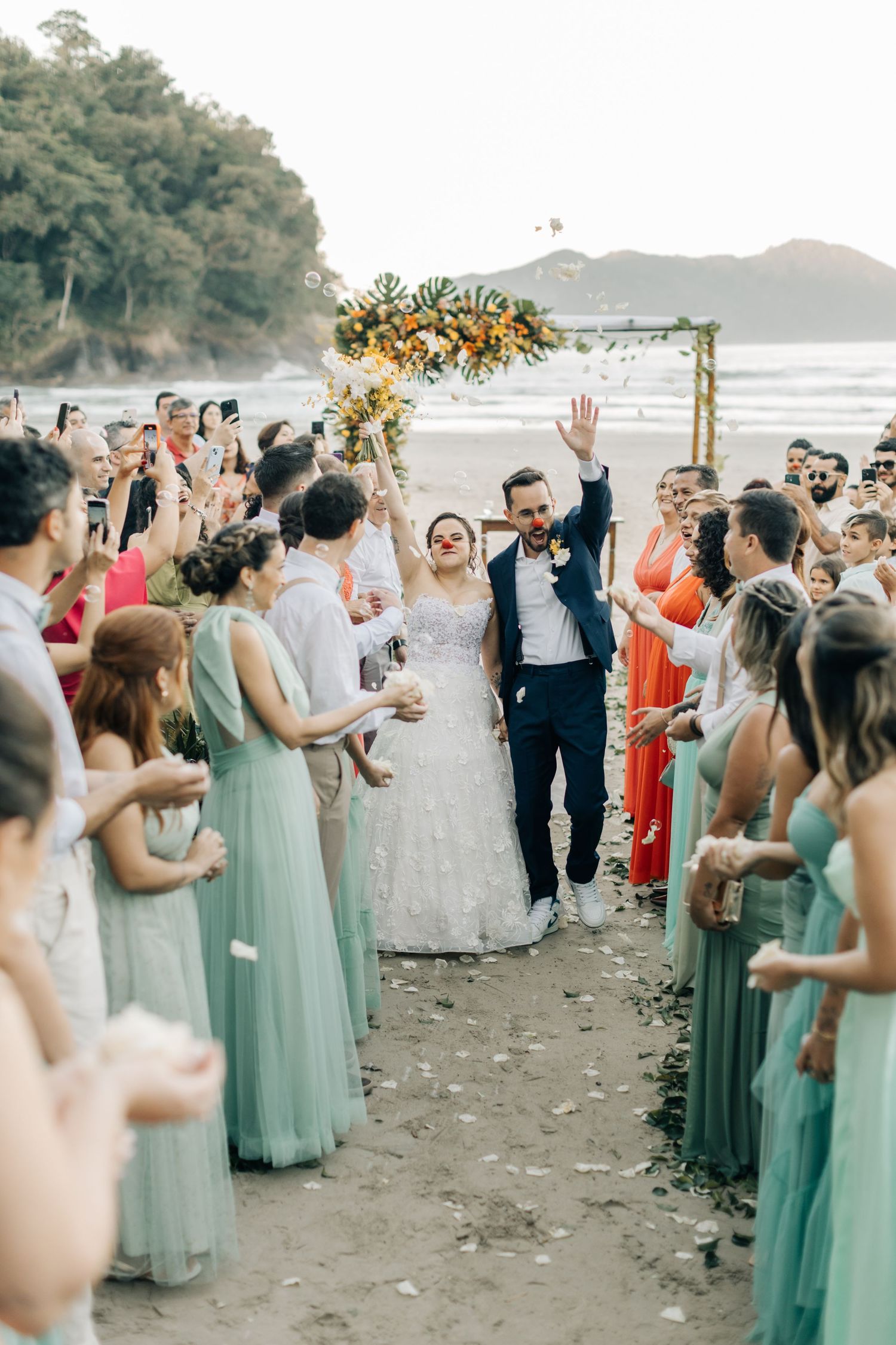 Wedding party exits beach ceremony through rows of guests in pastel dresses.