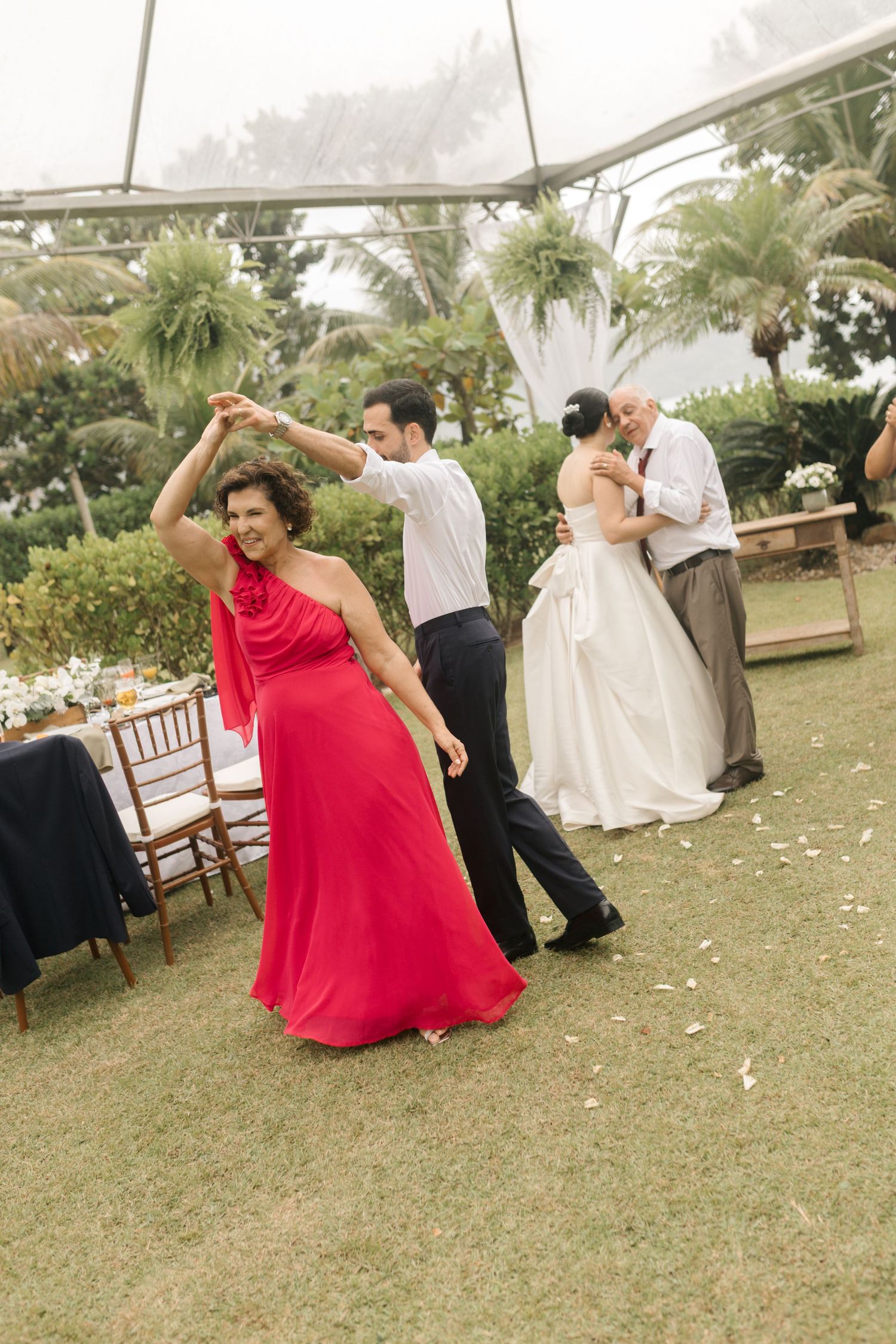 Wedding guests dancing at an outdoor reception with a bride and groom in the background.