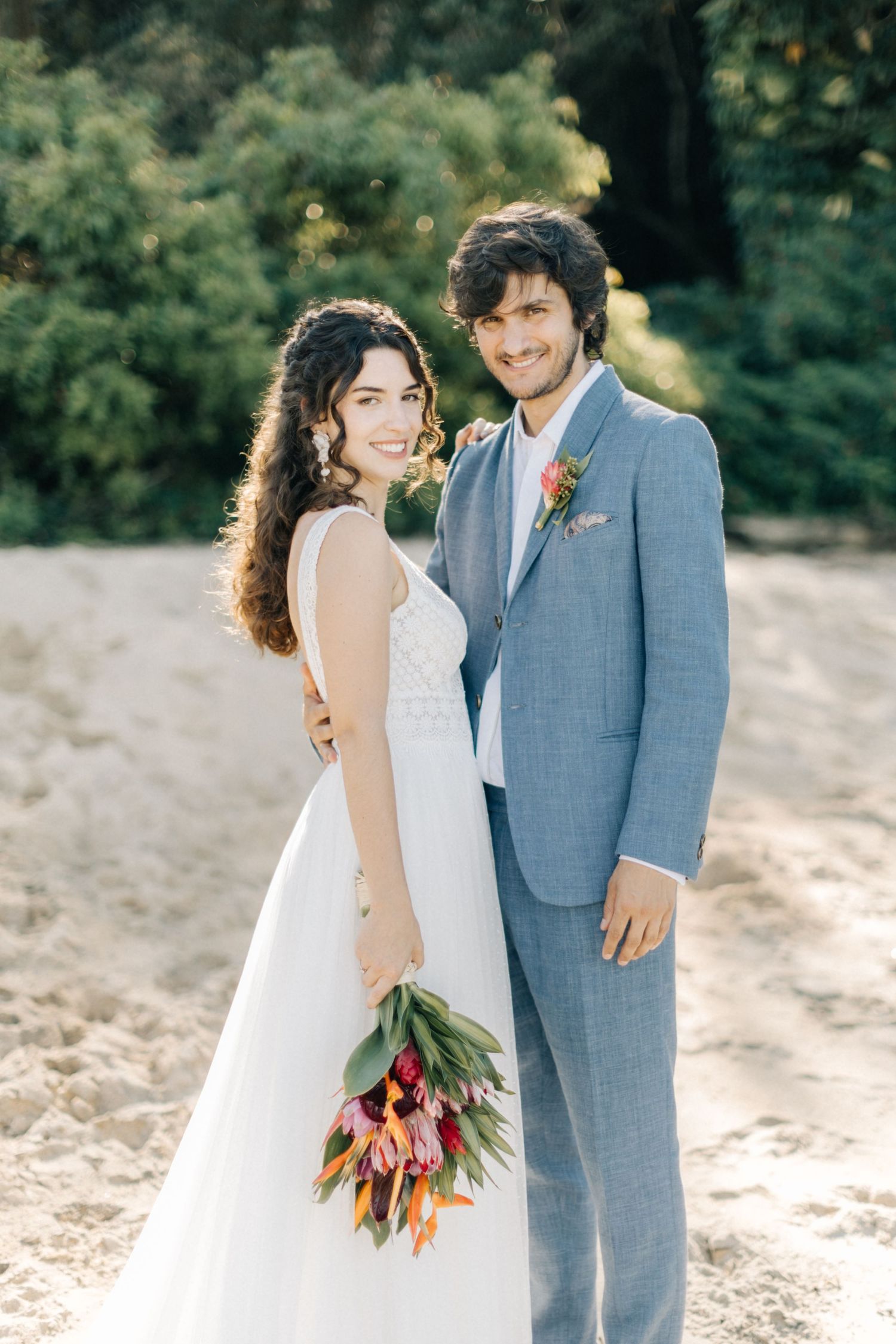 Newlyweds share intimate moment on beach with colorful tulip bouquet.