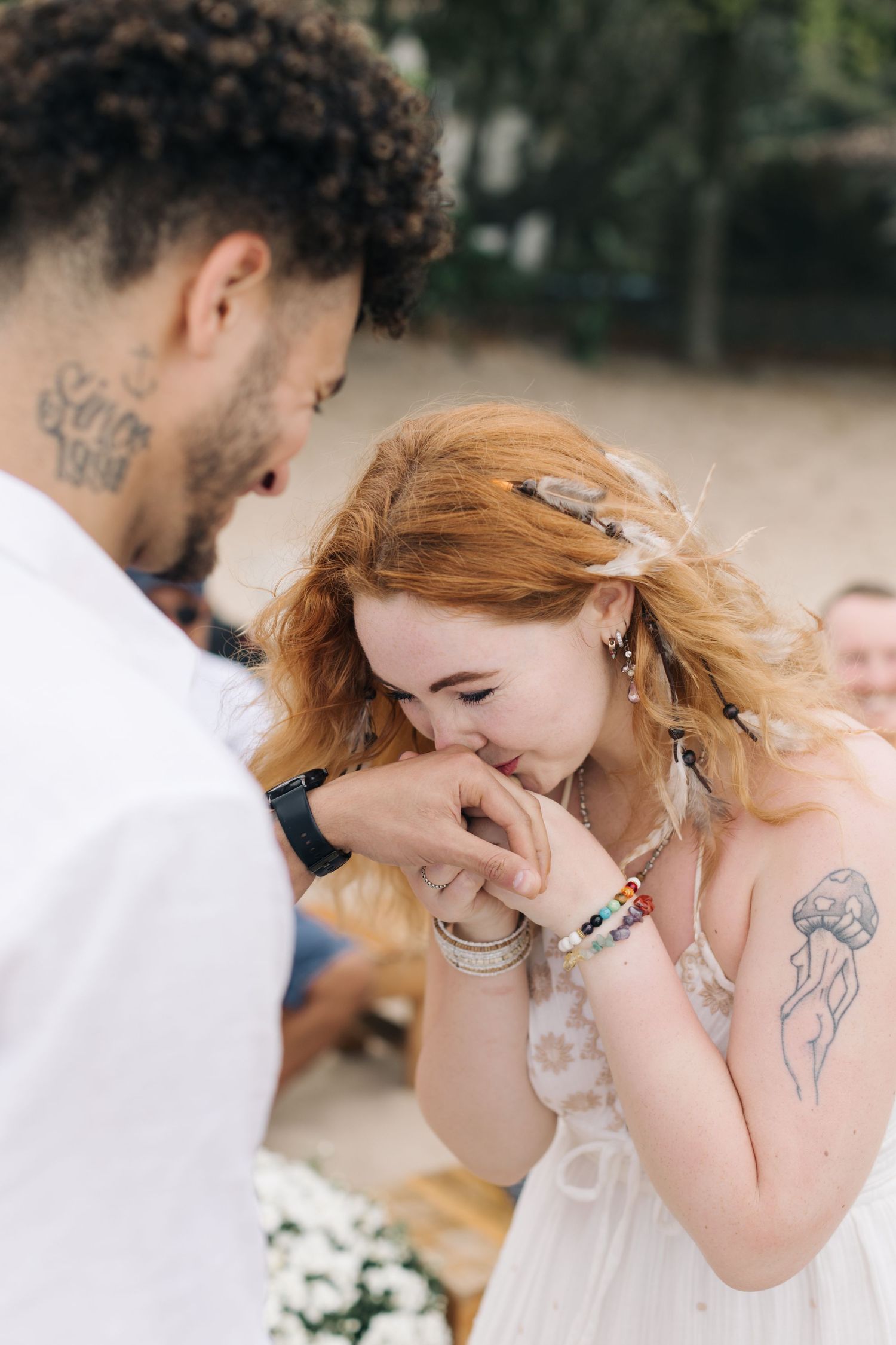 A touching moment during a beach wedding ceremony as a bride kisses her partner's hand amid natural lighting.
