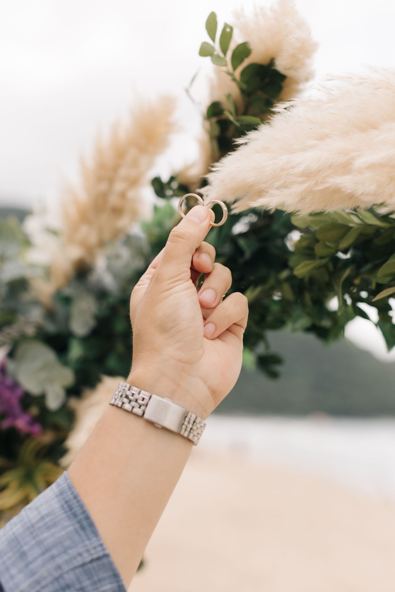 Detailed shot of hands wearing rings against a backdrop of pampas grass and greenery.