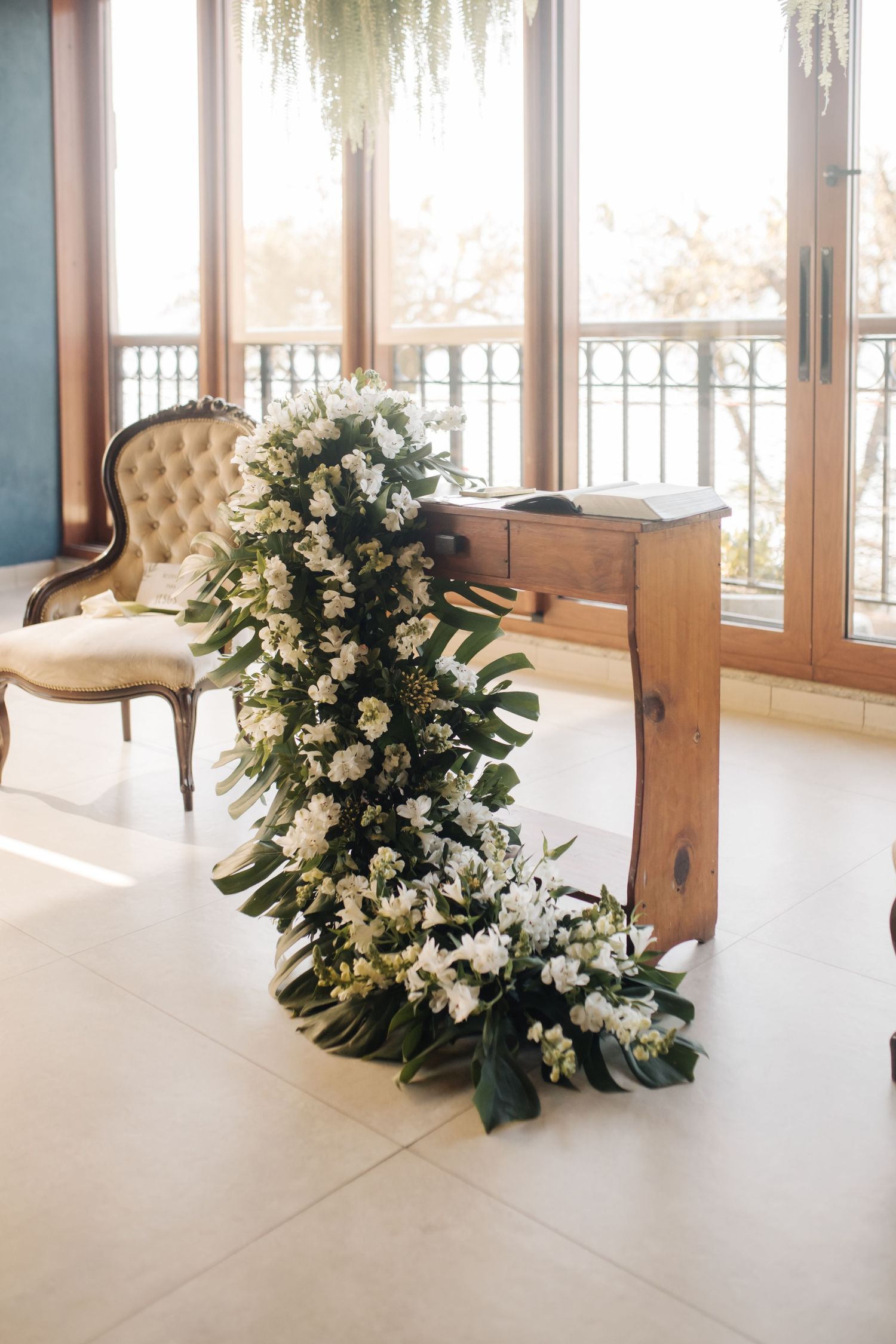 Bright wedding venue with cream tufted chairs and white floral arrangements.