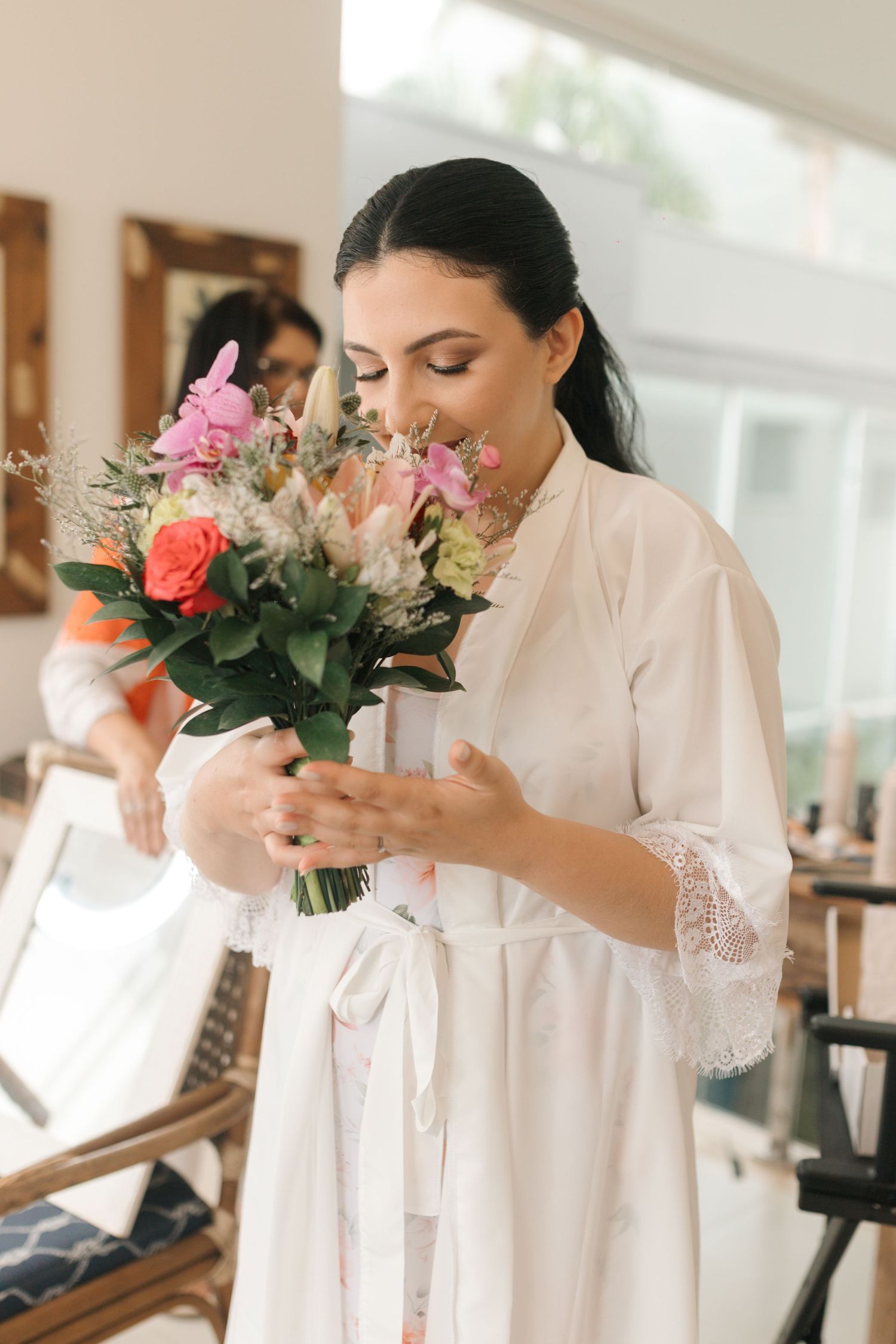 Woman in white dress smelling fresh bouquet of pink and coral flowers.