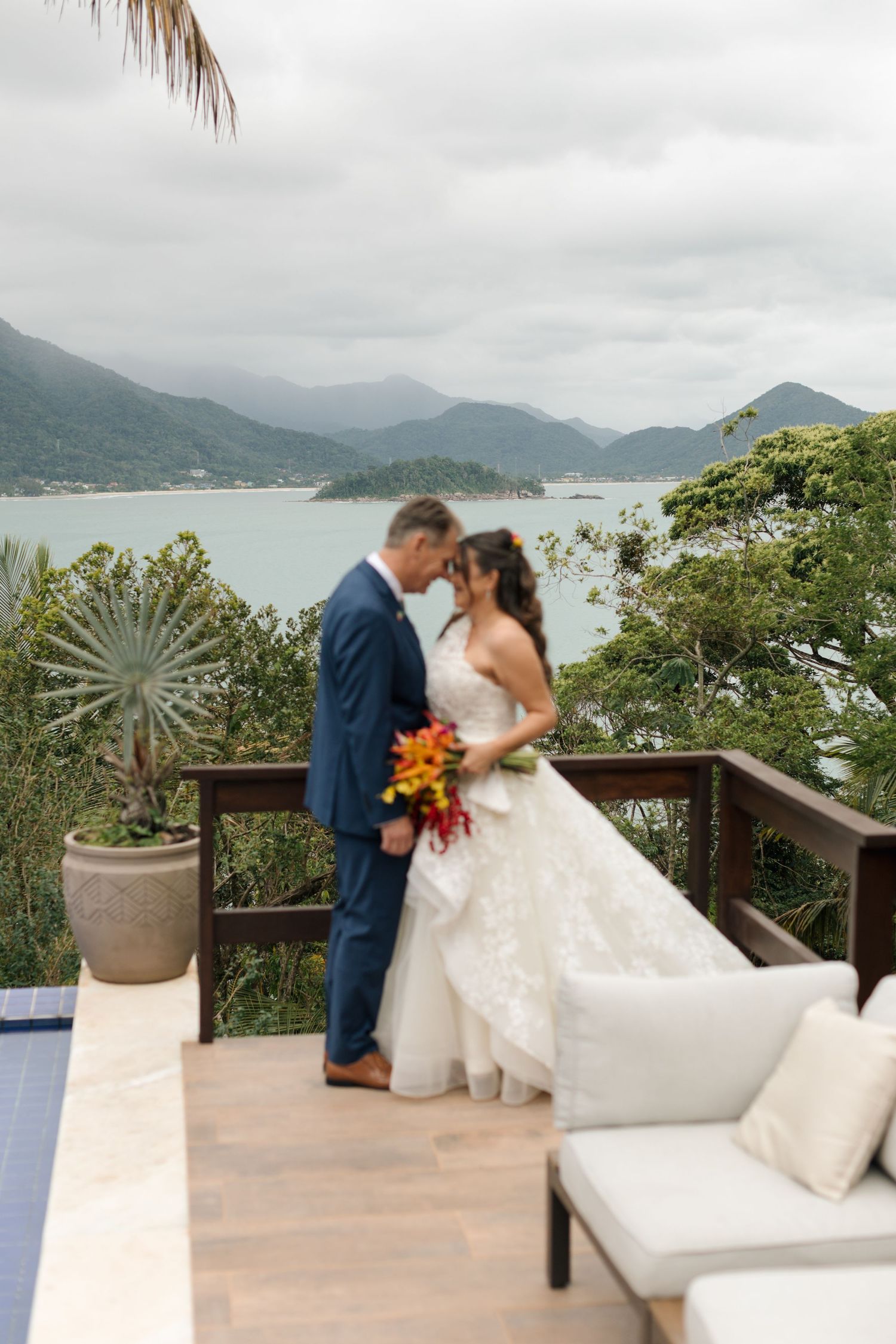 Scenic outdoor wedding venue overlooking mountains and ocean with tropical decor and white seating.