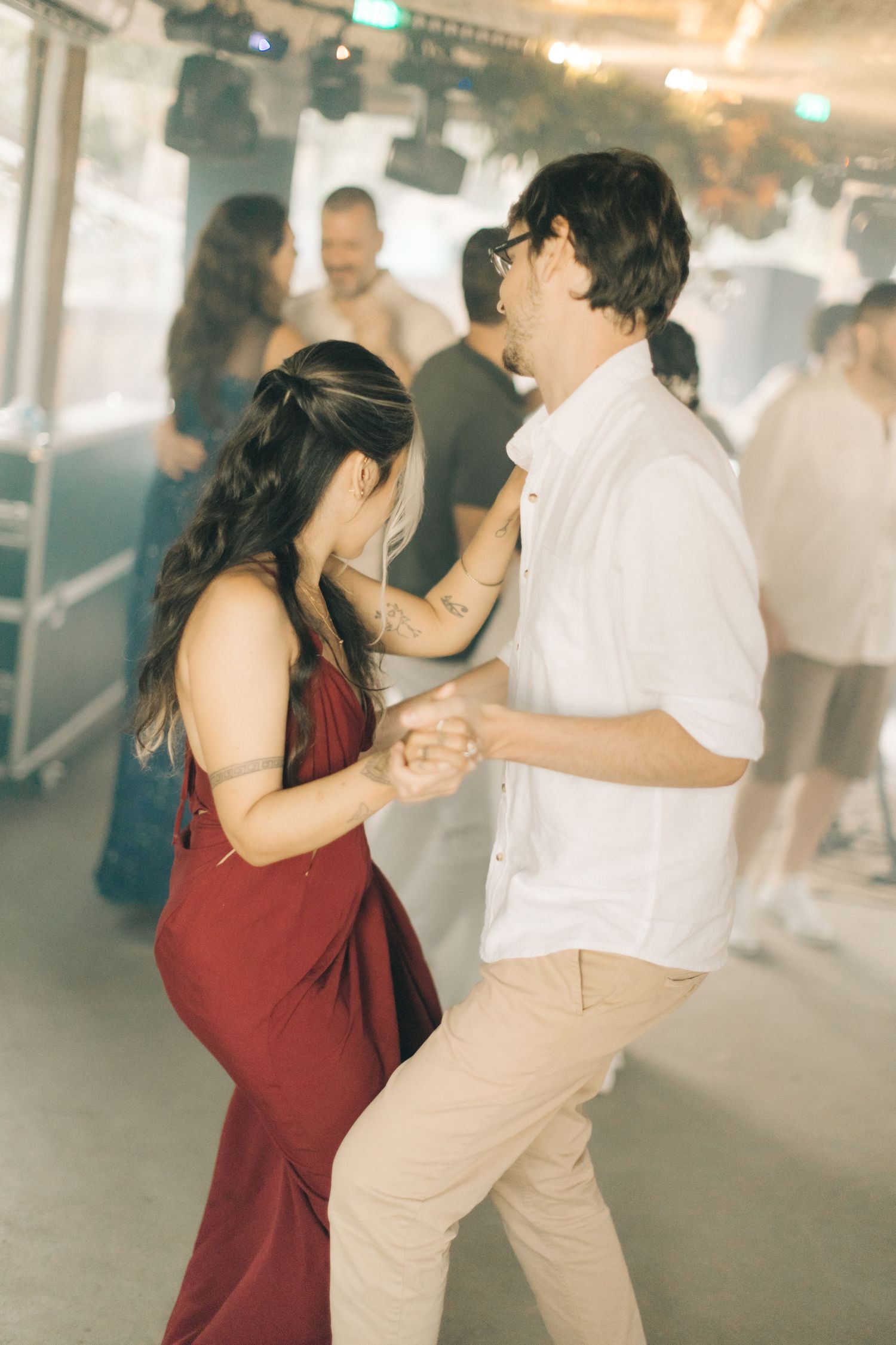 Couple dancing elegantly in burgundy and beige outfits at a social gathering.