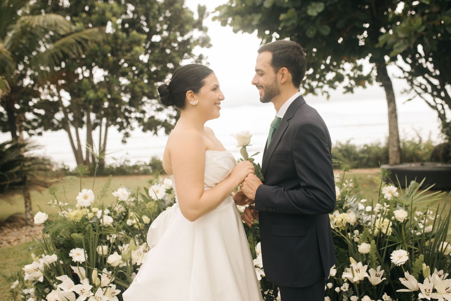 A joyful wedding couple shares a moment in a garden surrounded by white flowers.