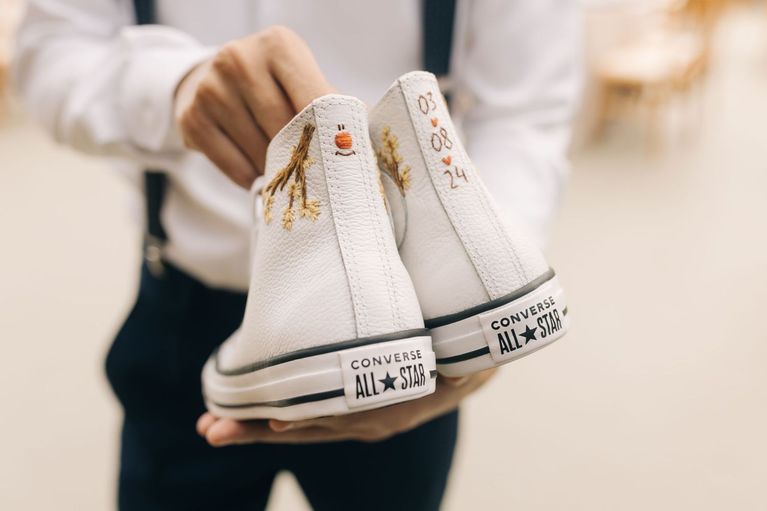 White Converse sneakers being held up as wedding shoes.
