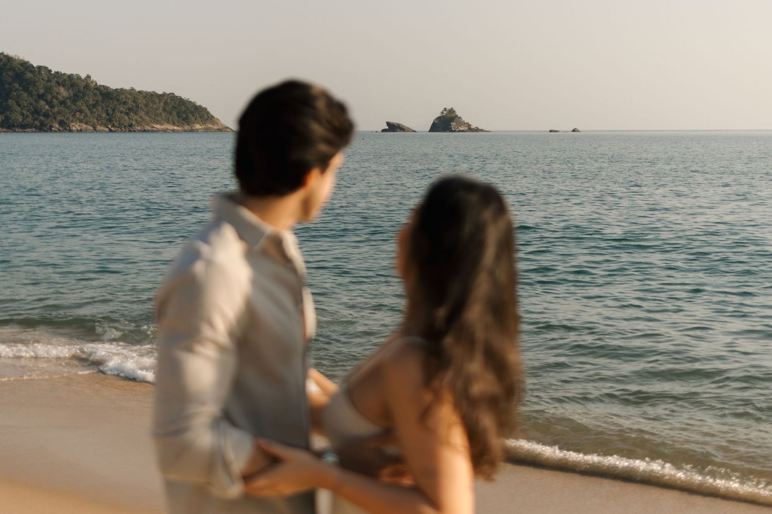 Two people walk hand in hand along a scenic ocean beach at sunset creating romantic silhouettes against the water.