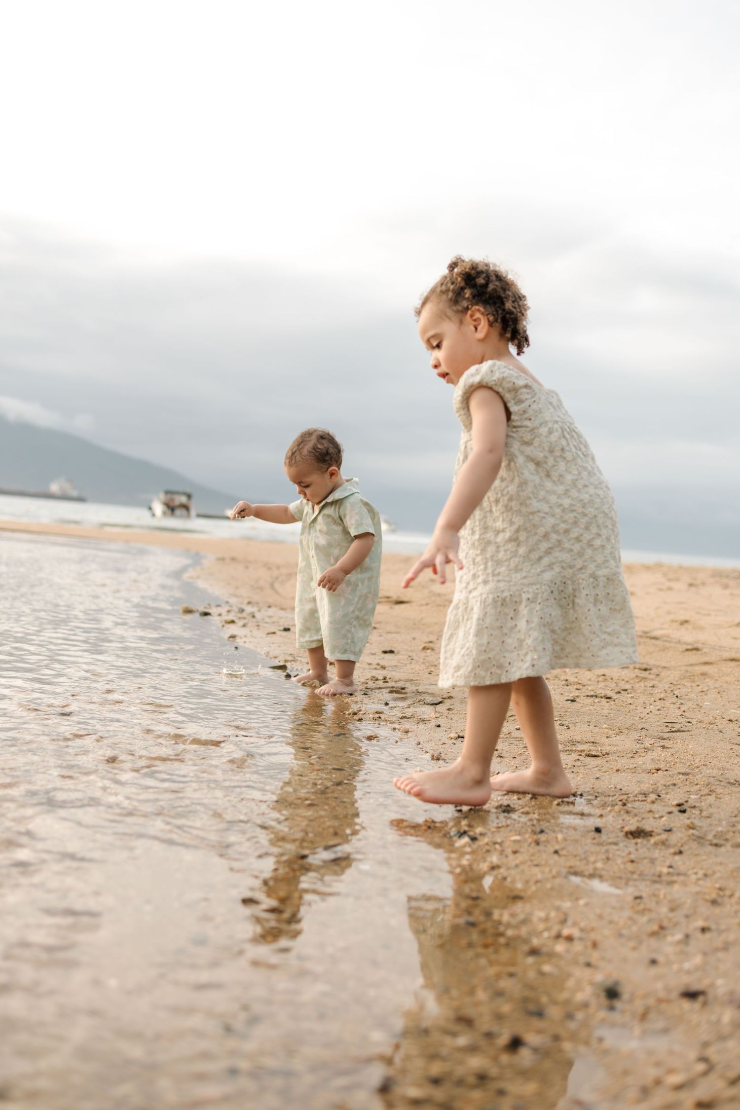 Children playing and splashing in the shallow waters at the beach during overcast weather.