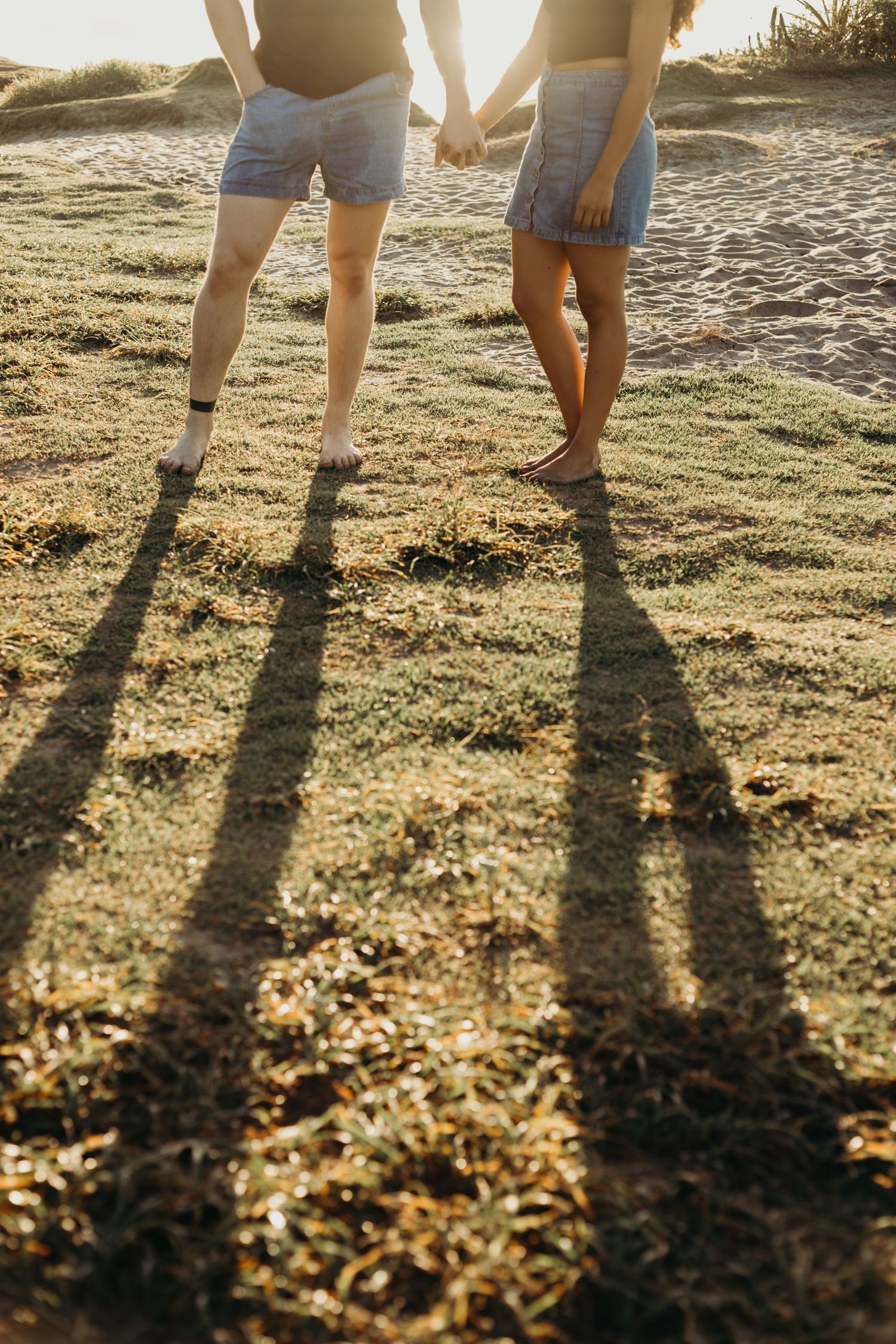 Long shadows cast by two people standing together on grassy coastal terrain at sunset.