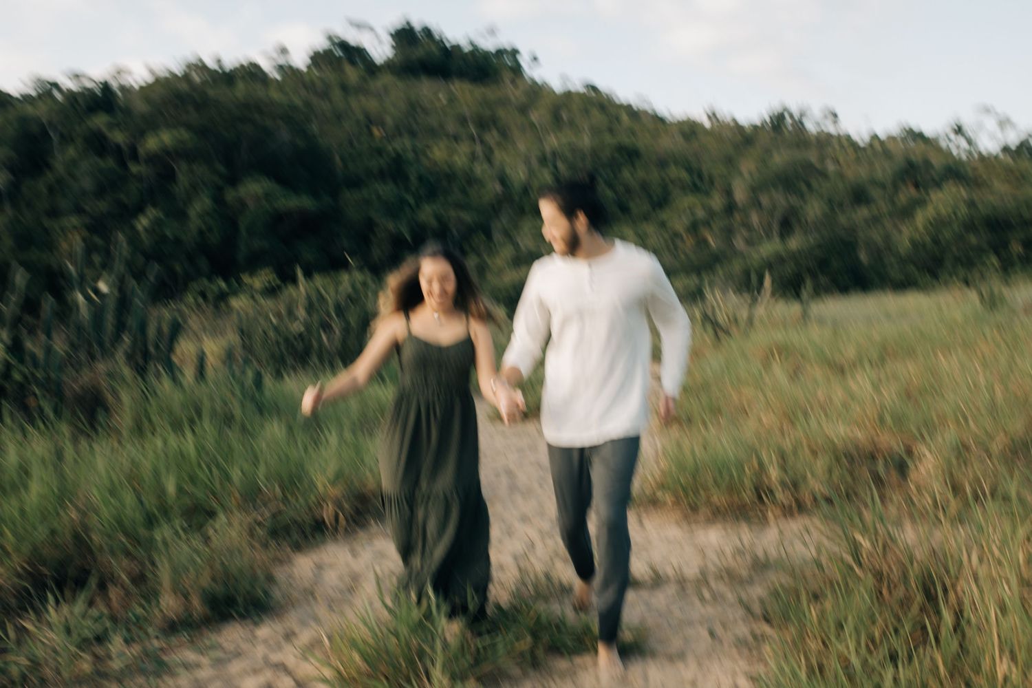 Couple runs hand-in-hand along a scenic nature trail surrounded by tall grass.