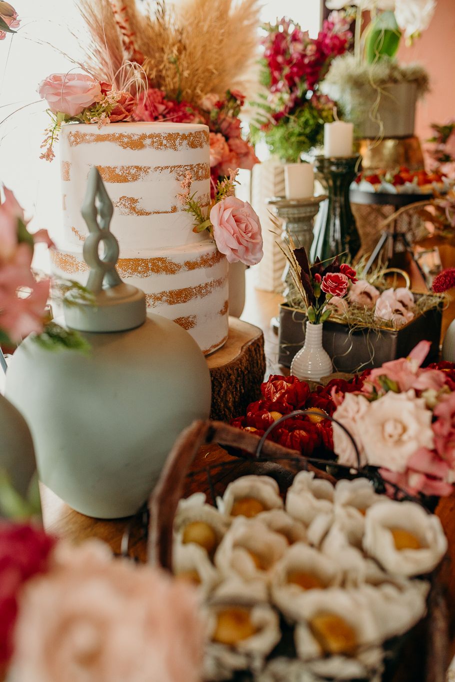 Wedding dessert table featuring tiered cake, vases with flowers, and rustic decorative elements.