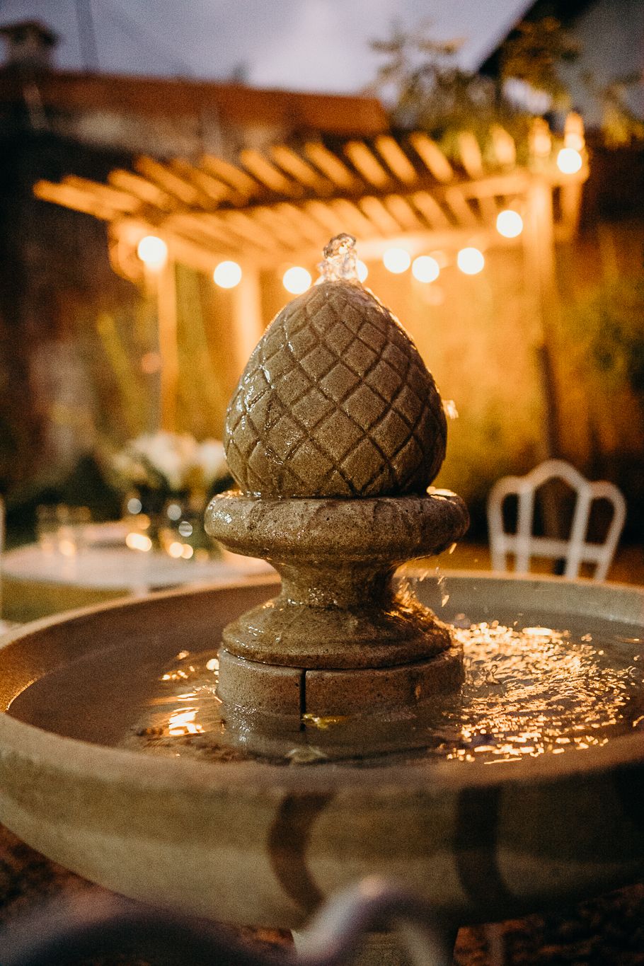 Decorative stone pineapple fountain illuminated by string lights at dusk.