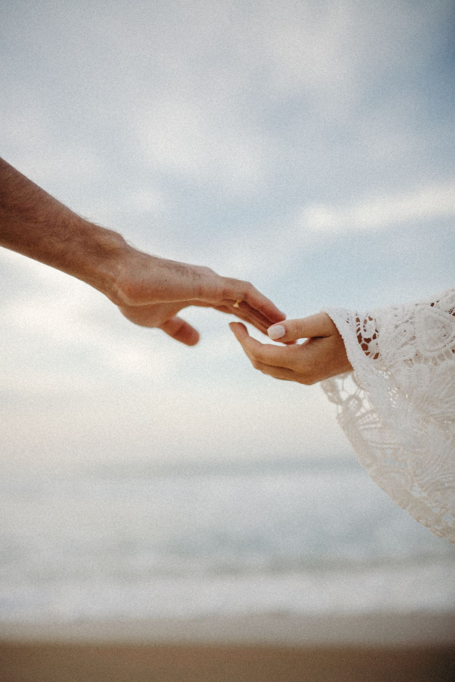 Close-up of hands reaching to touch against an ocean backdrop and cloudy sky.