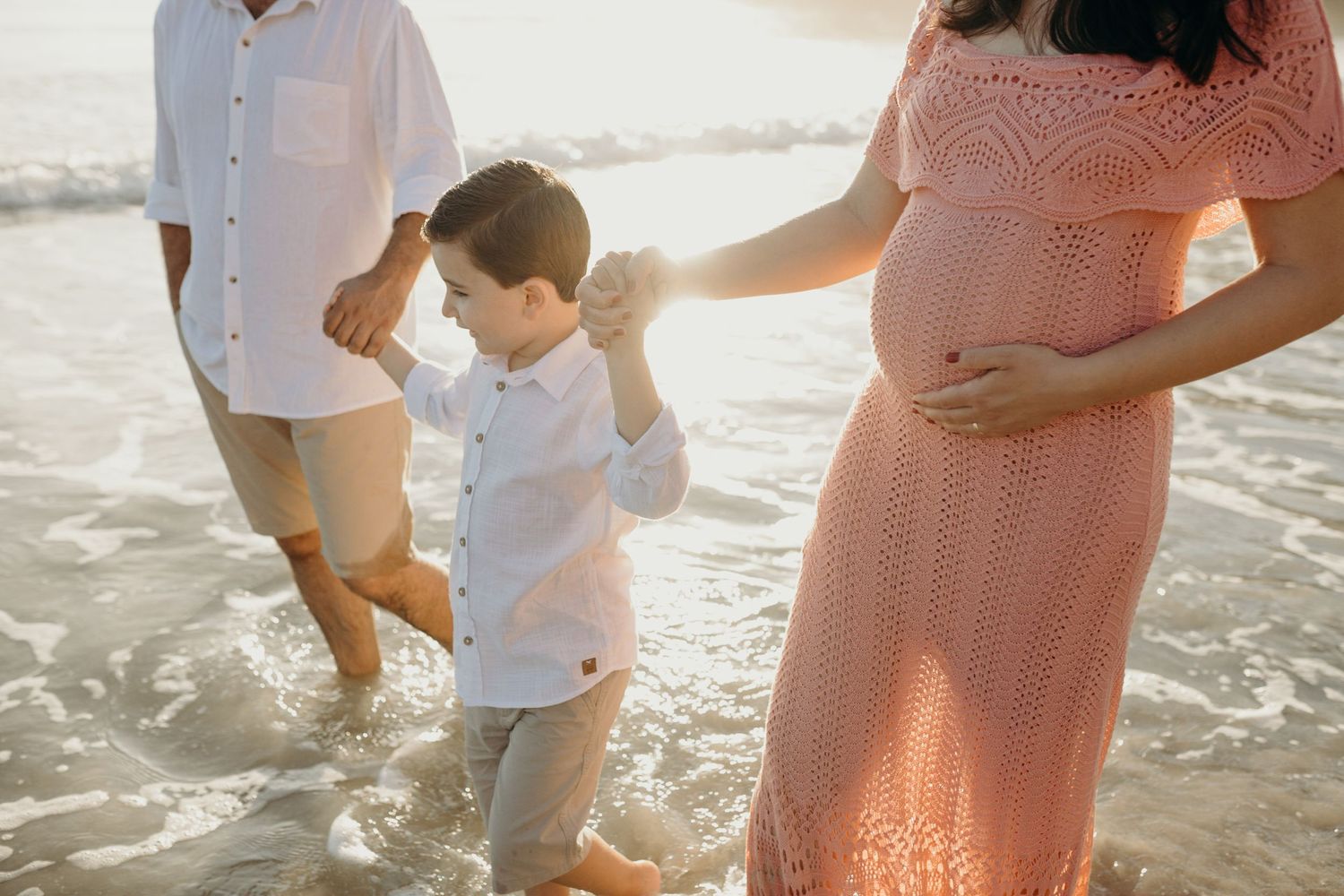 Family members walking barefoot in shallow ocean water during golden hour.