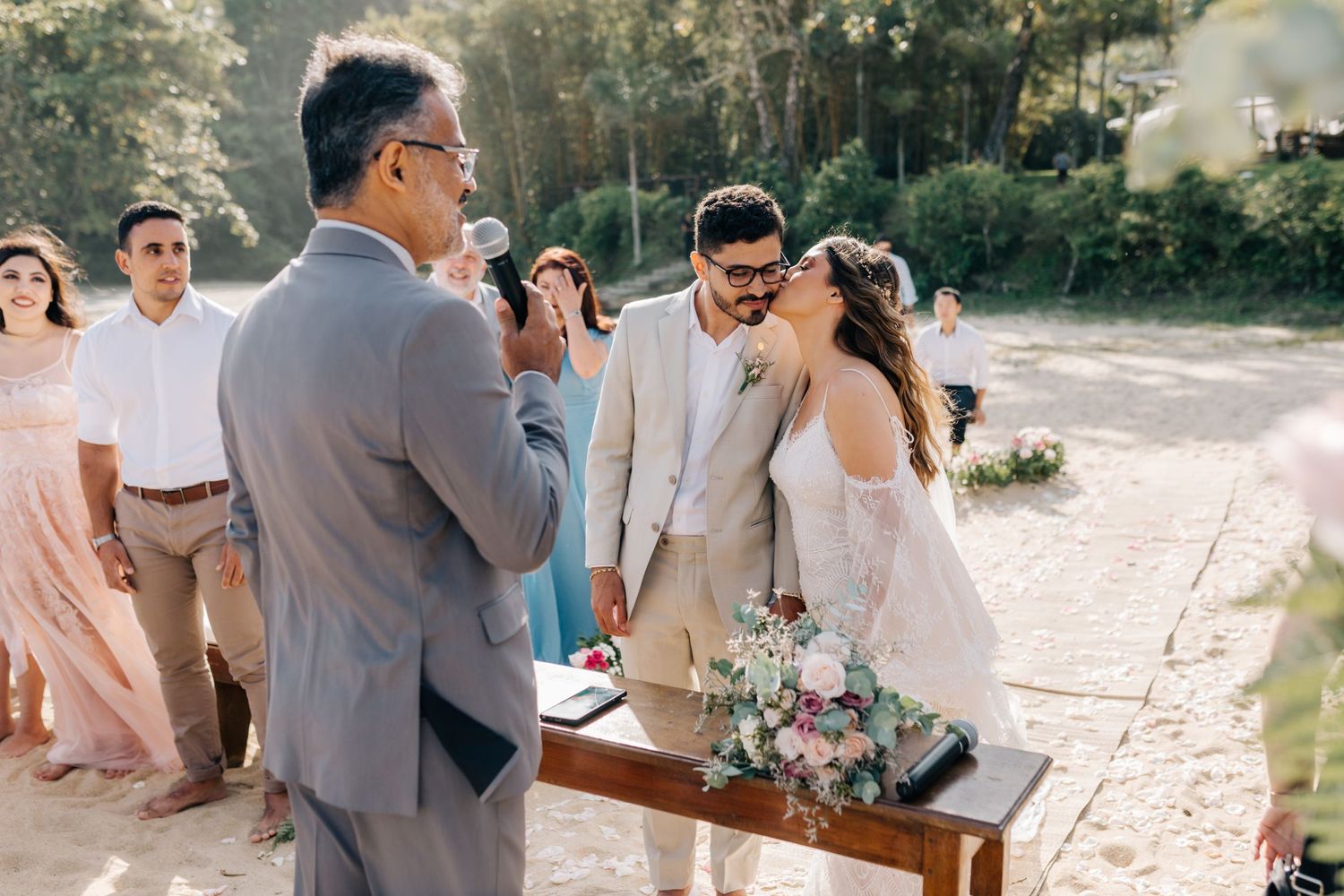 Wedding ceremony taking place on sandy beach path surrounded by greenery.