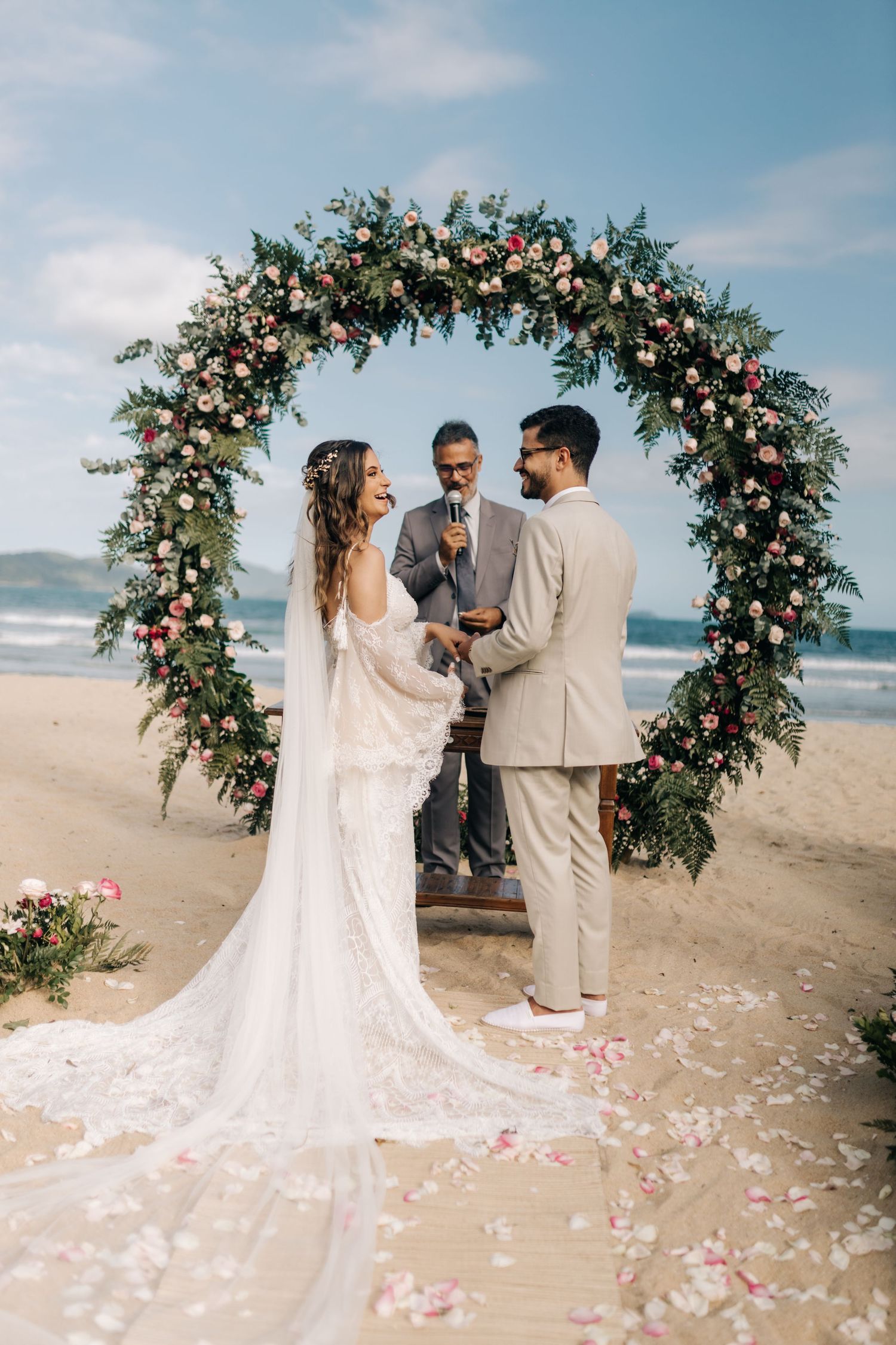 A wedding ceremony under a lush floral arch with ocean waves in the background.