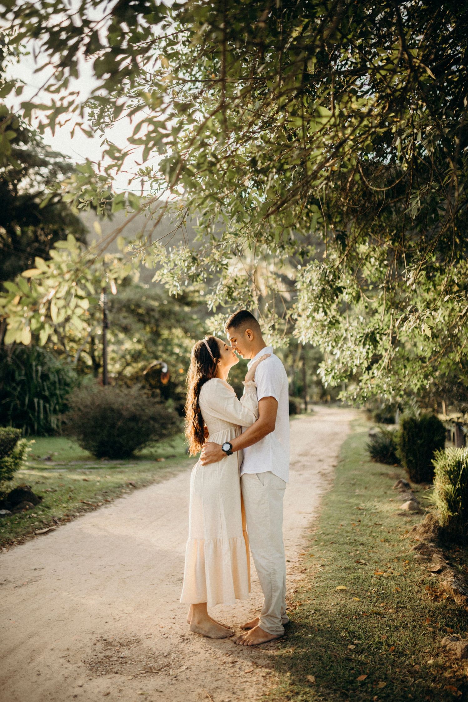 Romantic couple shares tender moments along a tree-lined path at golden hour.