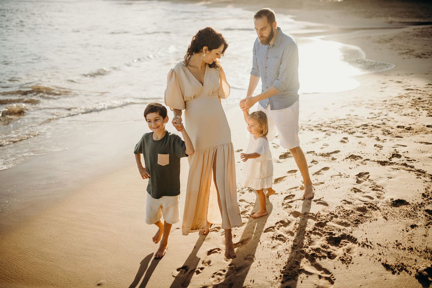 A family walks barefoot along the beach during a warm sunset evening.