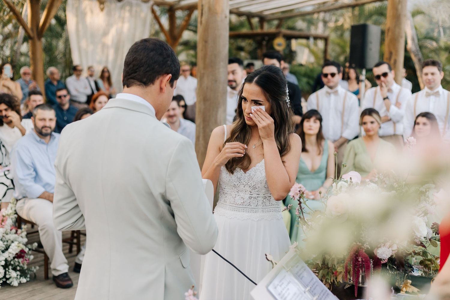 An emotional wedding ceremony moment captured between a couple in white attire with guests watching.