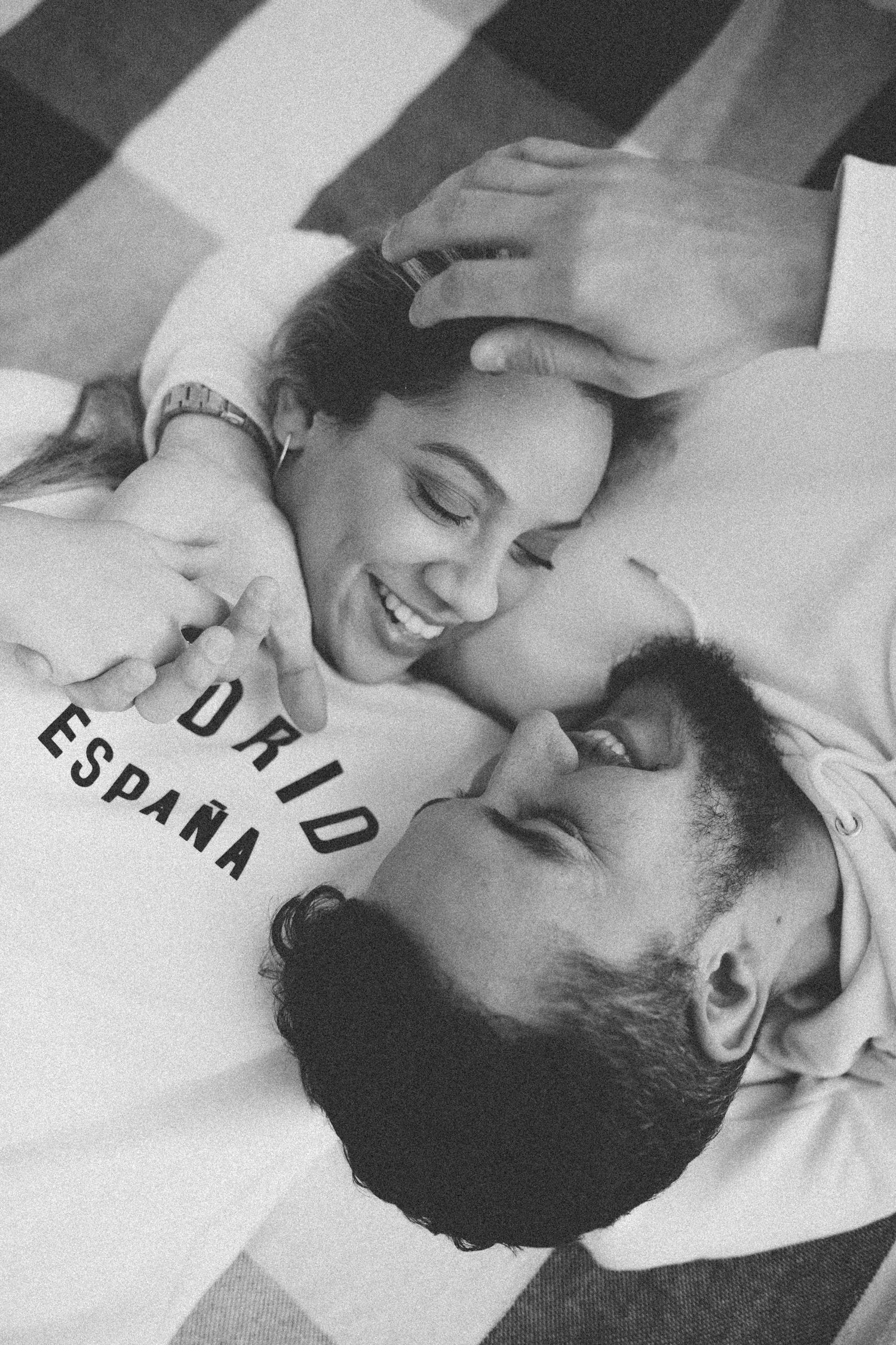 Black and white photo of couple smiling while lying on plaid blanket.
